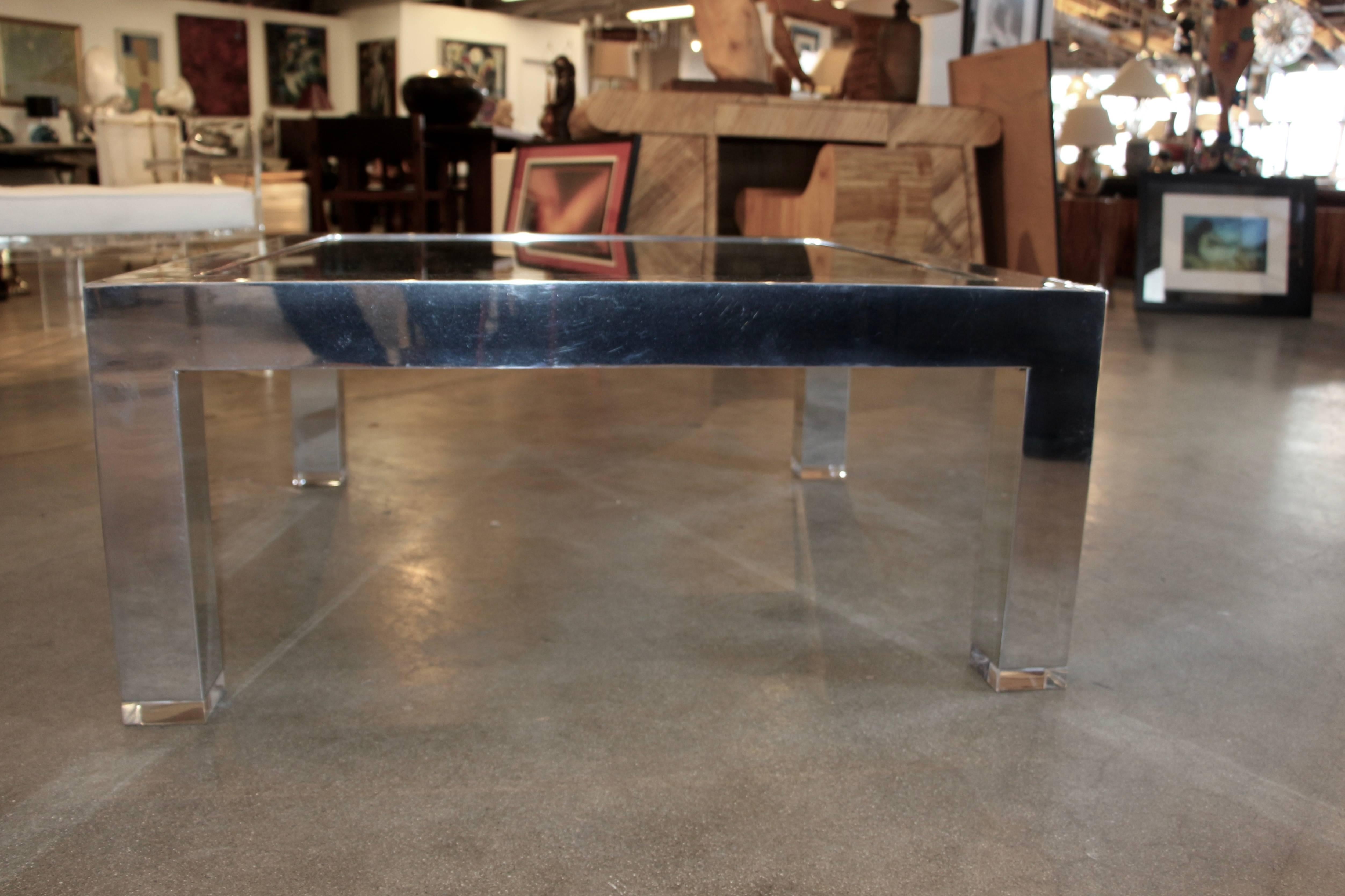 A lovely mirrored polished aluminium table with a glass inset. It features a nice touch with one inch Lucite feet.
