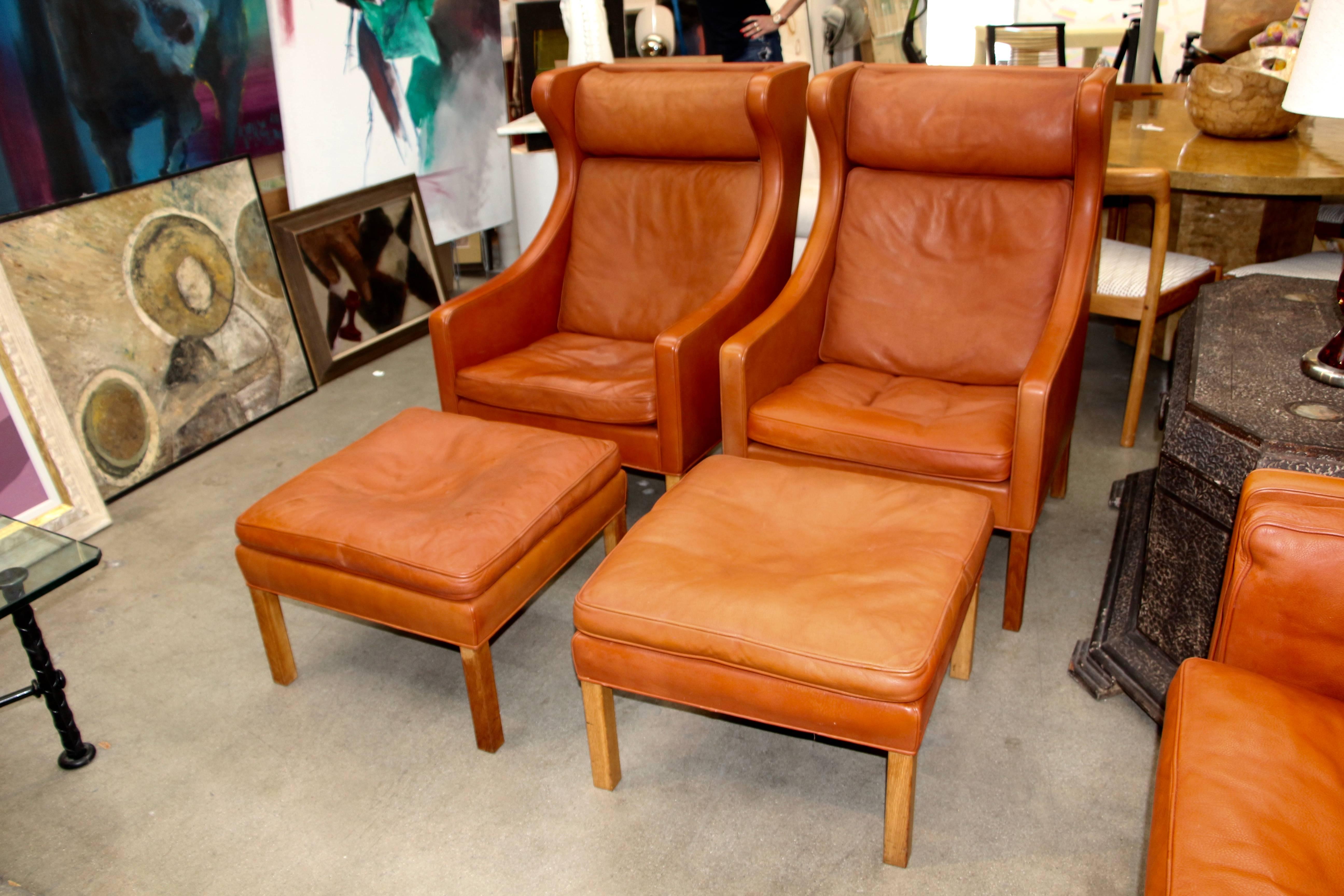 A pair of vintage leather wingback chairs designed in 1963 by Børge Mogensen for Fredericia Furniture of Denmark. Based on the labels on the ottomans and chairs, we date these to the 1960s and this was verified by the estate we purchased these from.