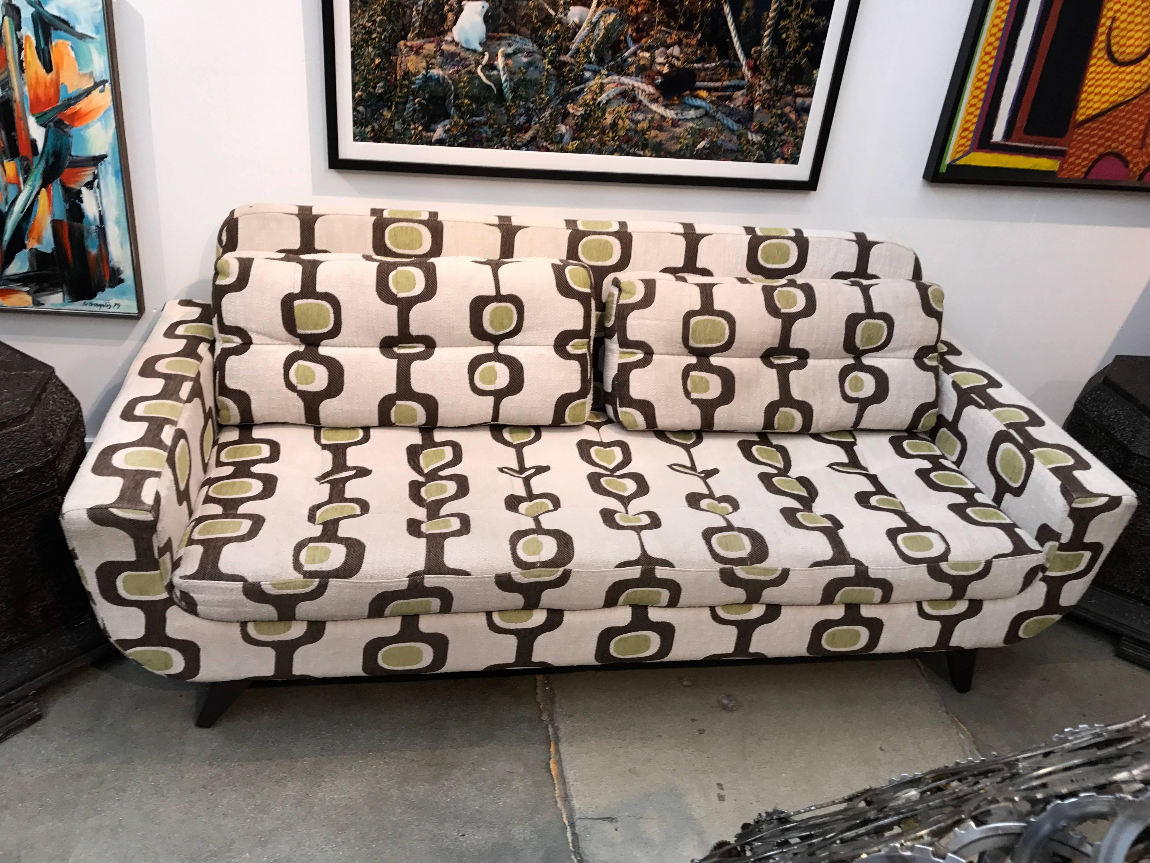 A quite unusual sofa in its original fabric. No idea as to the designer. We have left the original fabric although it could use a cleaning. The worst of area is pictured on the right top cushions. Nice angled legs, painted brown. Comfortable as well.