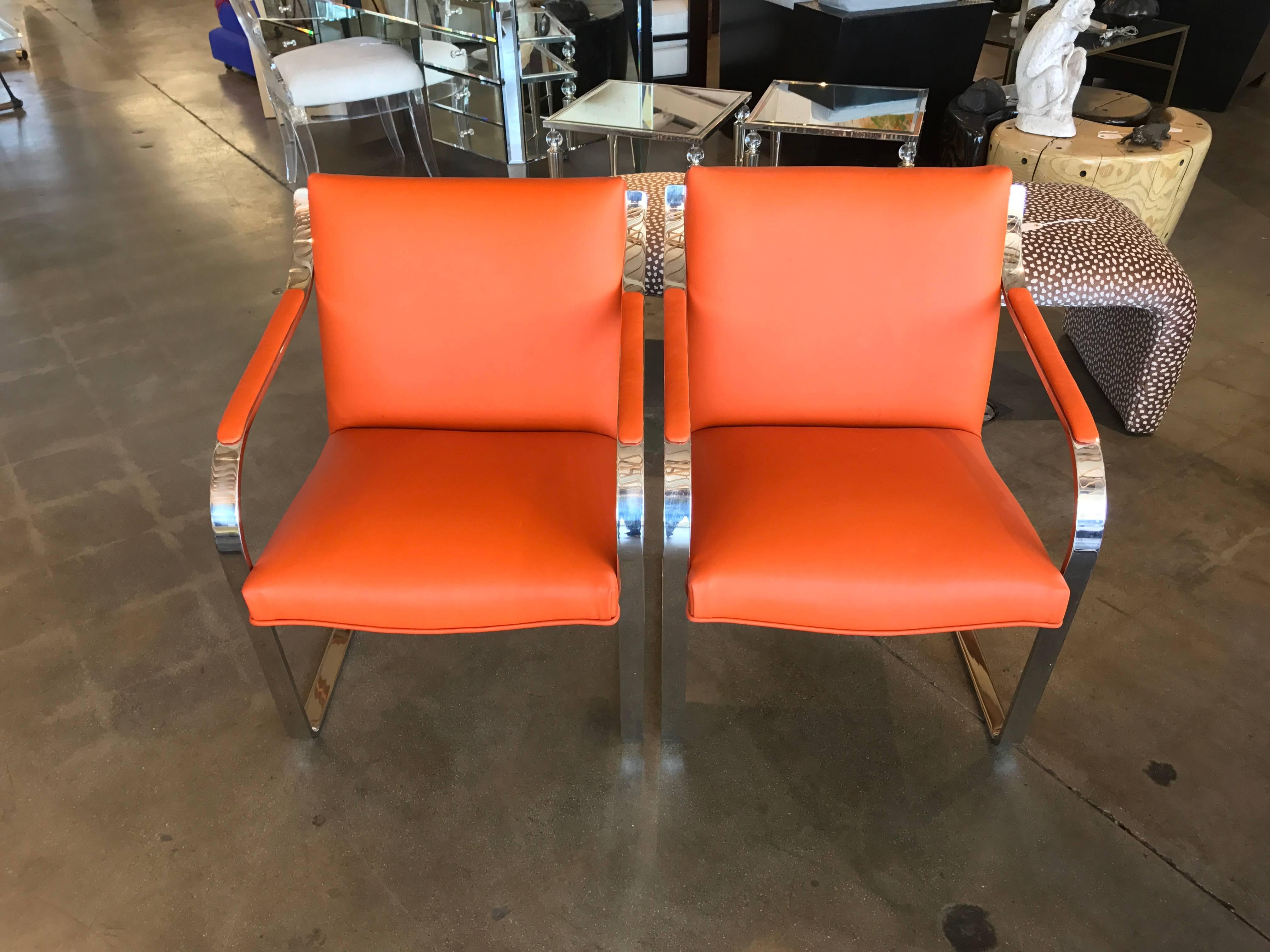 A nice older pair of Brueton Brno type chairs redone in a Hermes tone orange leather of nice quality. The chairs are slightly different in the way they have survived as one is a little more give in it, please see the photos. They are structurally