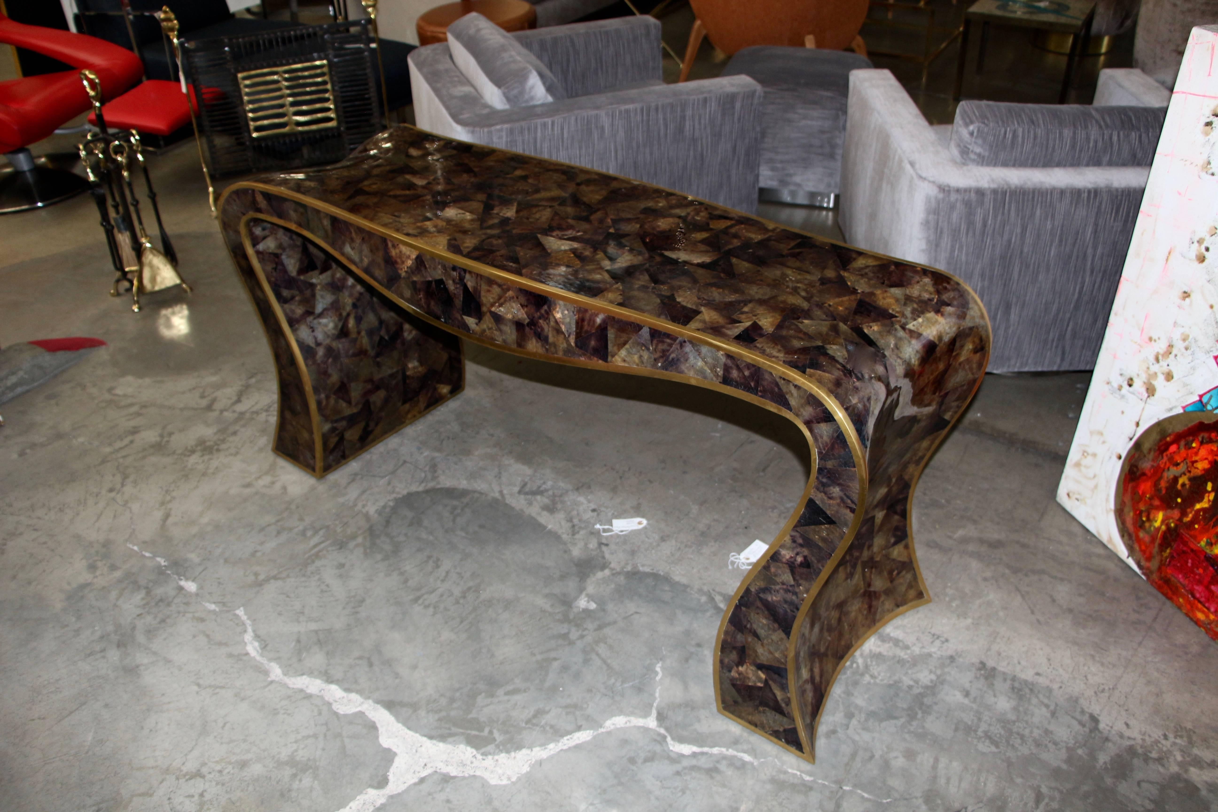 A quite stunning sculptural console table bearing a Maitland-Smith label on the underside. There is a natural craquelure to the lacquer finish. It is tessellated Horn with brass trim in a sinuous form. A very striking table. There are minor losses