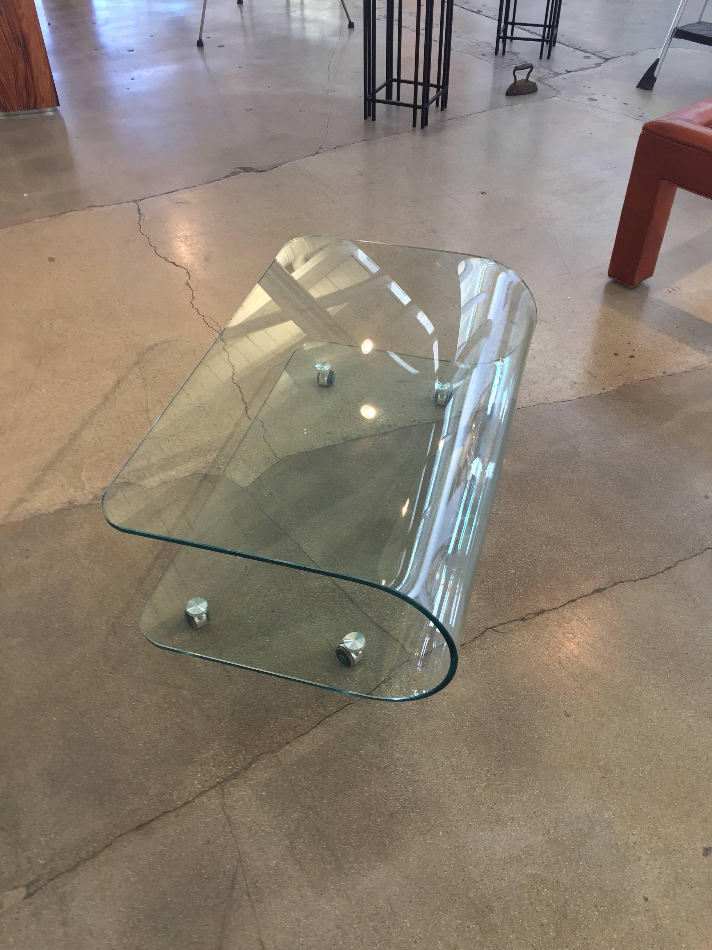 A pretty unique sculptural curved glass coffee or multifunction table. It is on lockable castors and rolls freely when unlocked. In excellent condition.