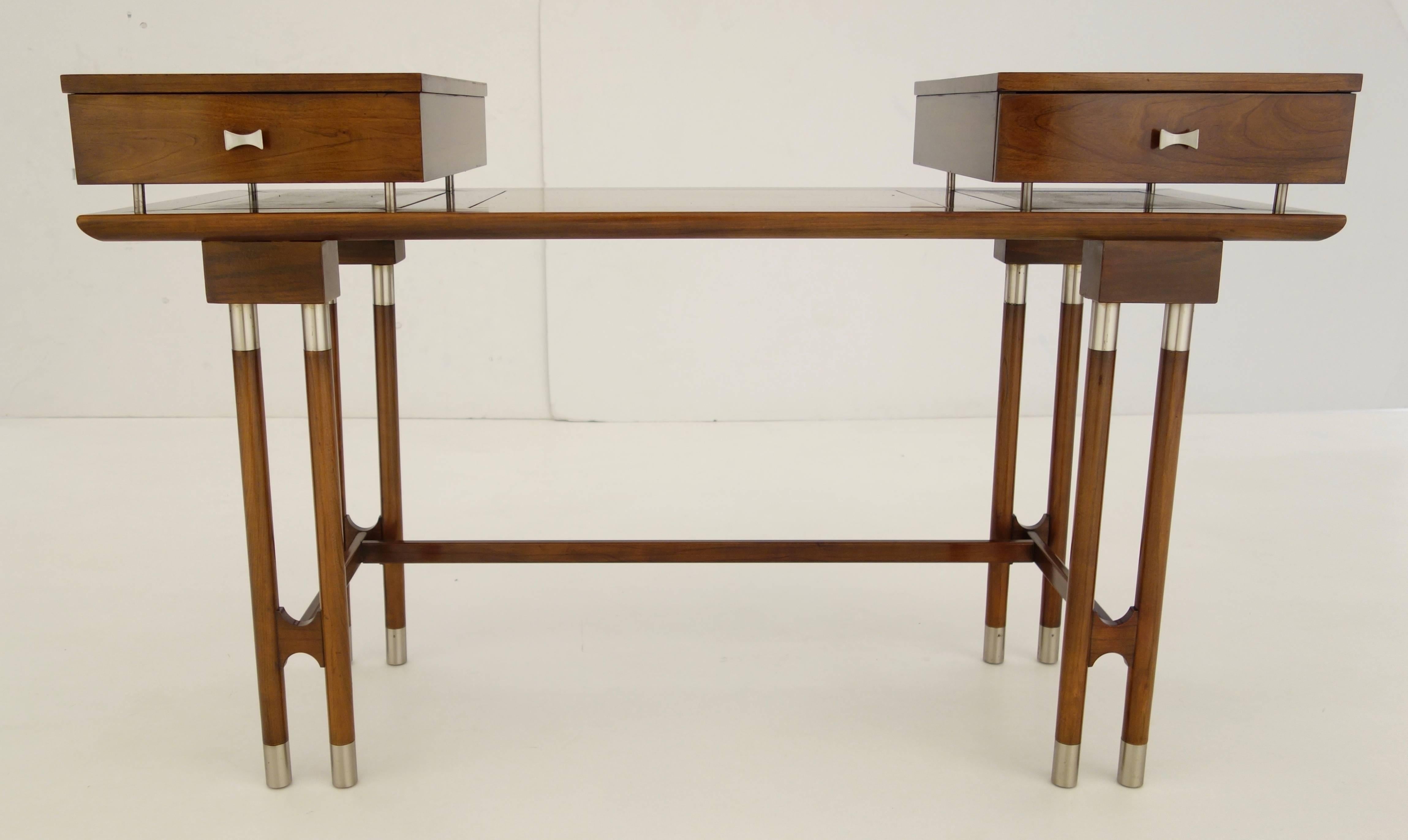 A Mid-Century writing desk or vanity, the top featuring two pull-out drawers floating on the flat surface comprised of three inset lighter wood panels resting on eight tubular legs capped at both ends with nickel hardware connected by two short and