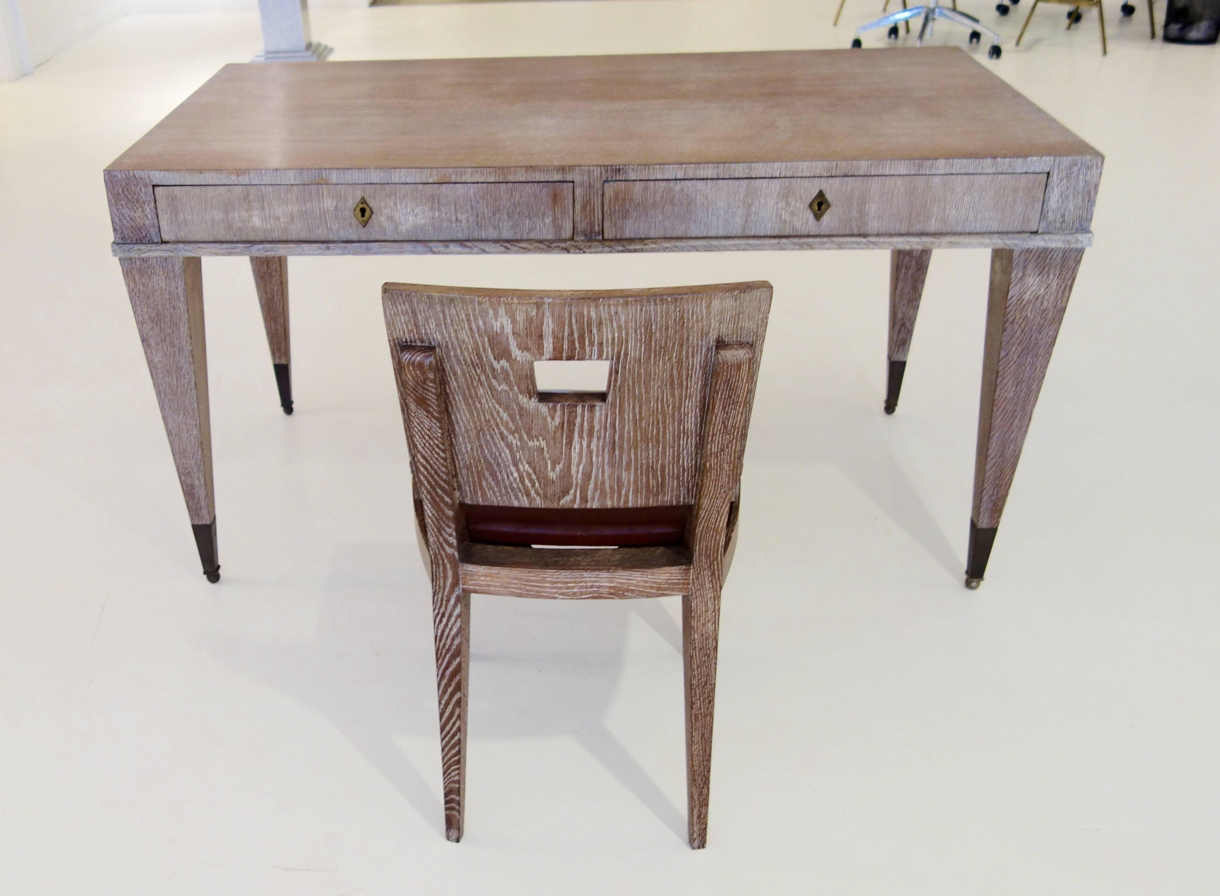 A French Mid-Century oak writing desk, the rectangular top with two pull-out drawers with brass diamond shaped escutcheons surmounted on four sided tapered brass capped legs raised on balls. The matching chair with rectangular pierced back and