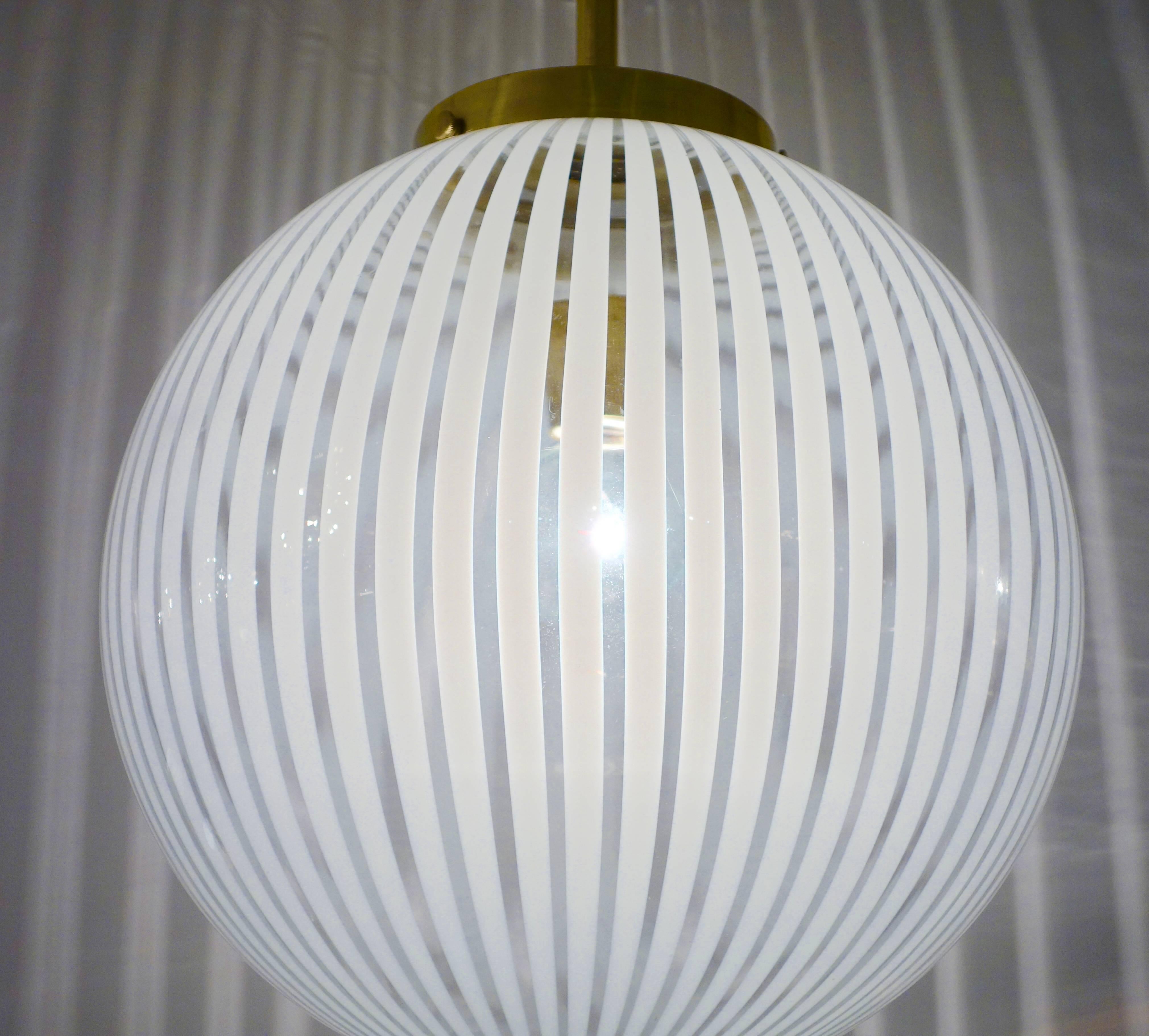 An Italian Mid-Century handblown Murano glass globe, chandelier or pendant featuring white opaque vertical stripes on clear class suspended by a contemporary custom tapered brass cone and canopy newly wired with a single brass socket that can