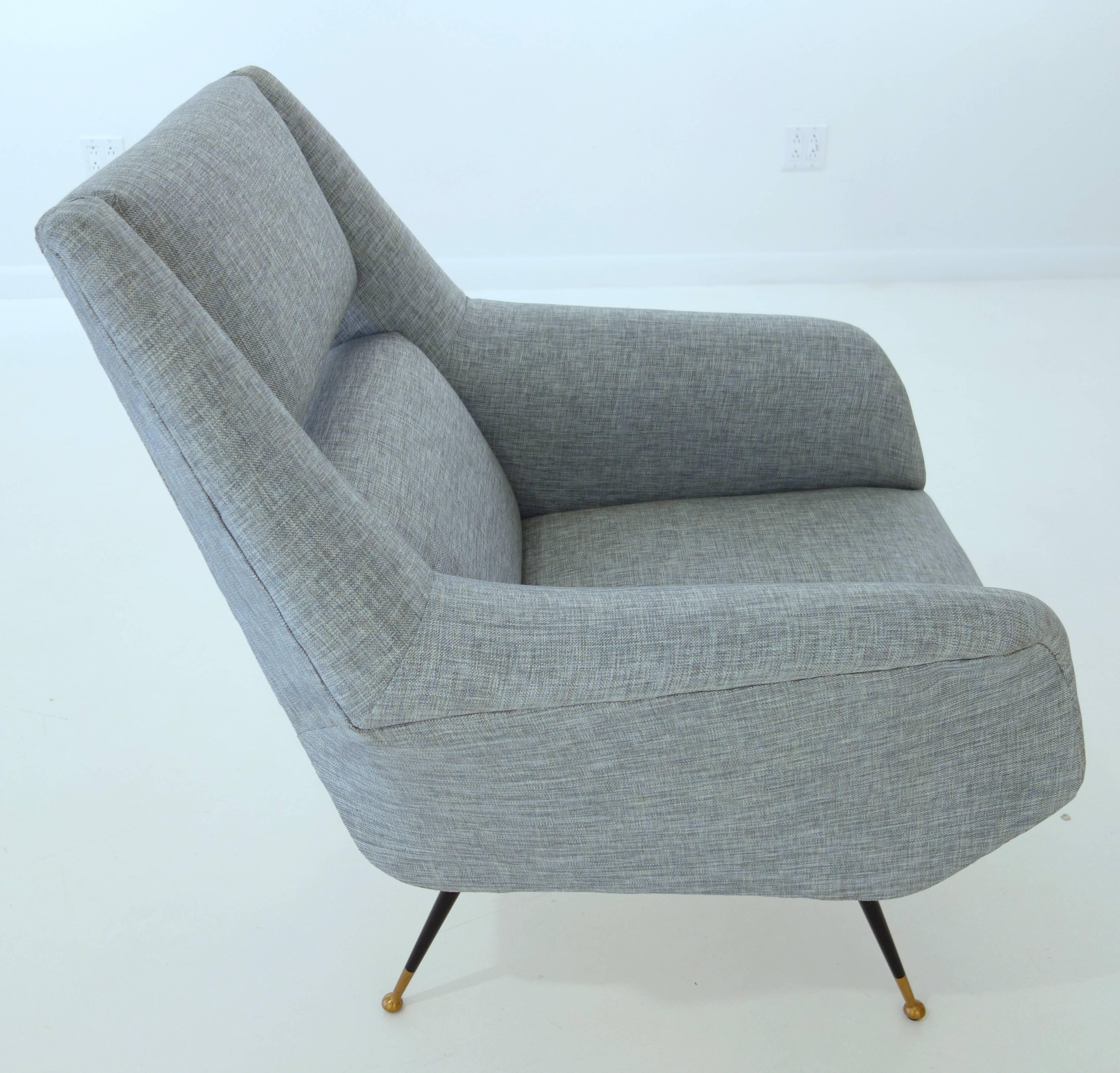 A pair of large Italian Mid-Century lounge or armchairs in the style of Carlo de Carli with cut-out backs and slightly flared arms with tight seats resting on black metal legs with brass caps newly upholstered in woven slate blue fabric with a