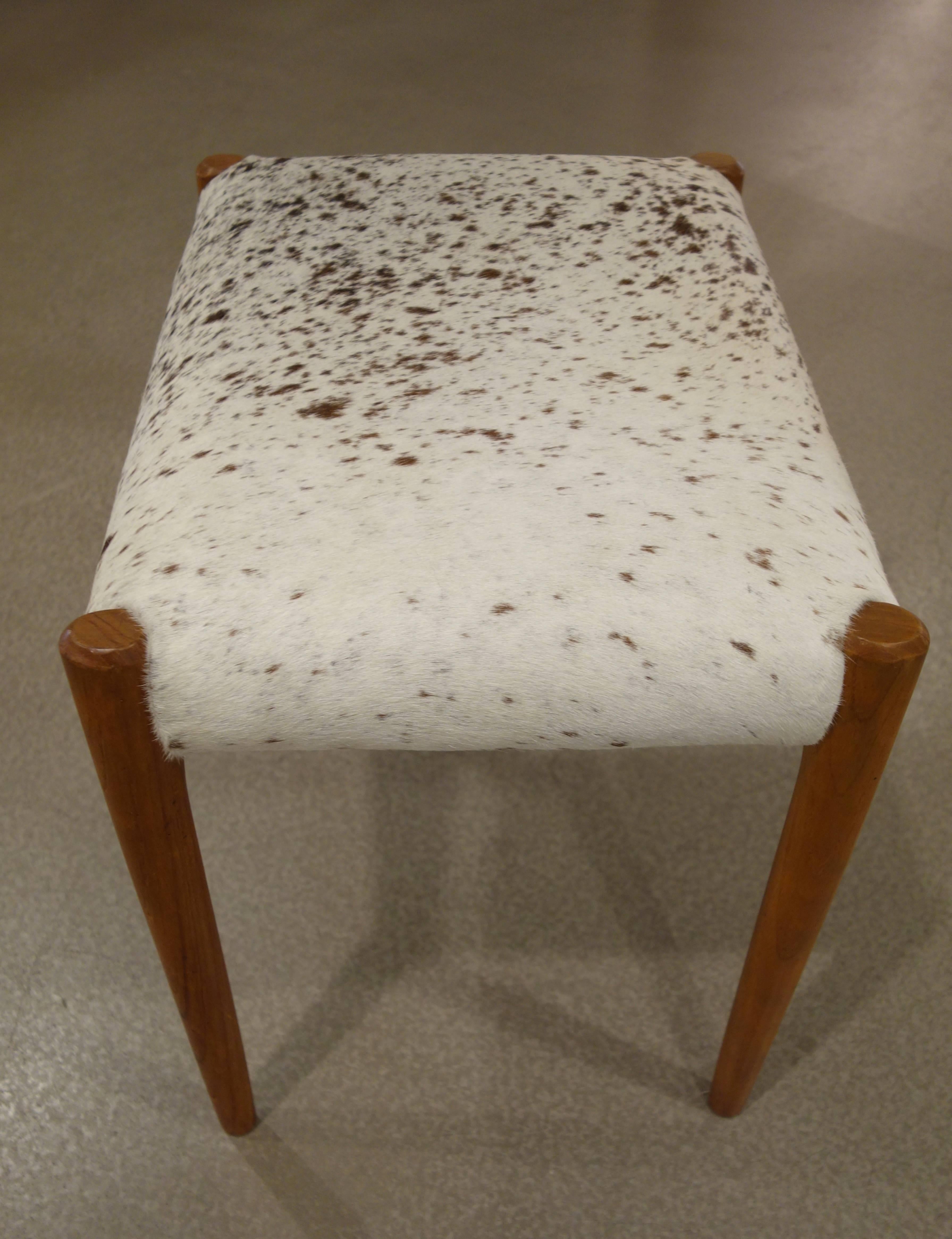 A pair of Mid-Century Danish stools by Niels O. Moller for J.L. Moller with tight newly upholstered seats in whiskey brown and white cowhide resting on honey colored teak wood.