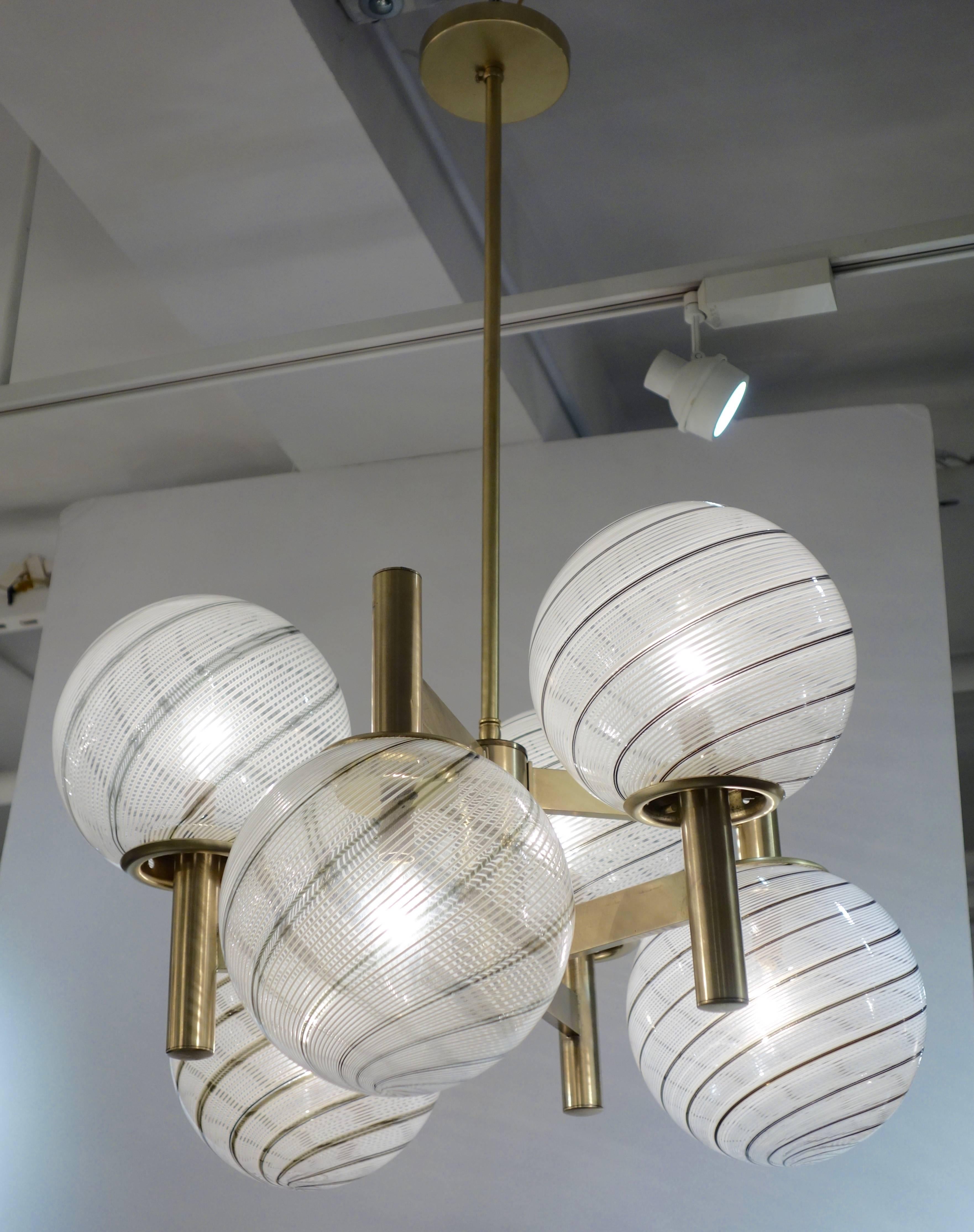 An Italian Mid-Century sculptural chandelier featuring six handblown Murano glass globes each a variation of clear with white and bronze to gray stripes with 3 downturned arms and 3 upturned, the frame re-plated in satin brass with 6 newly wired