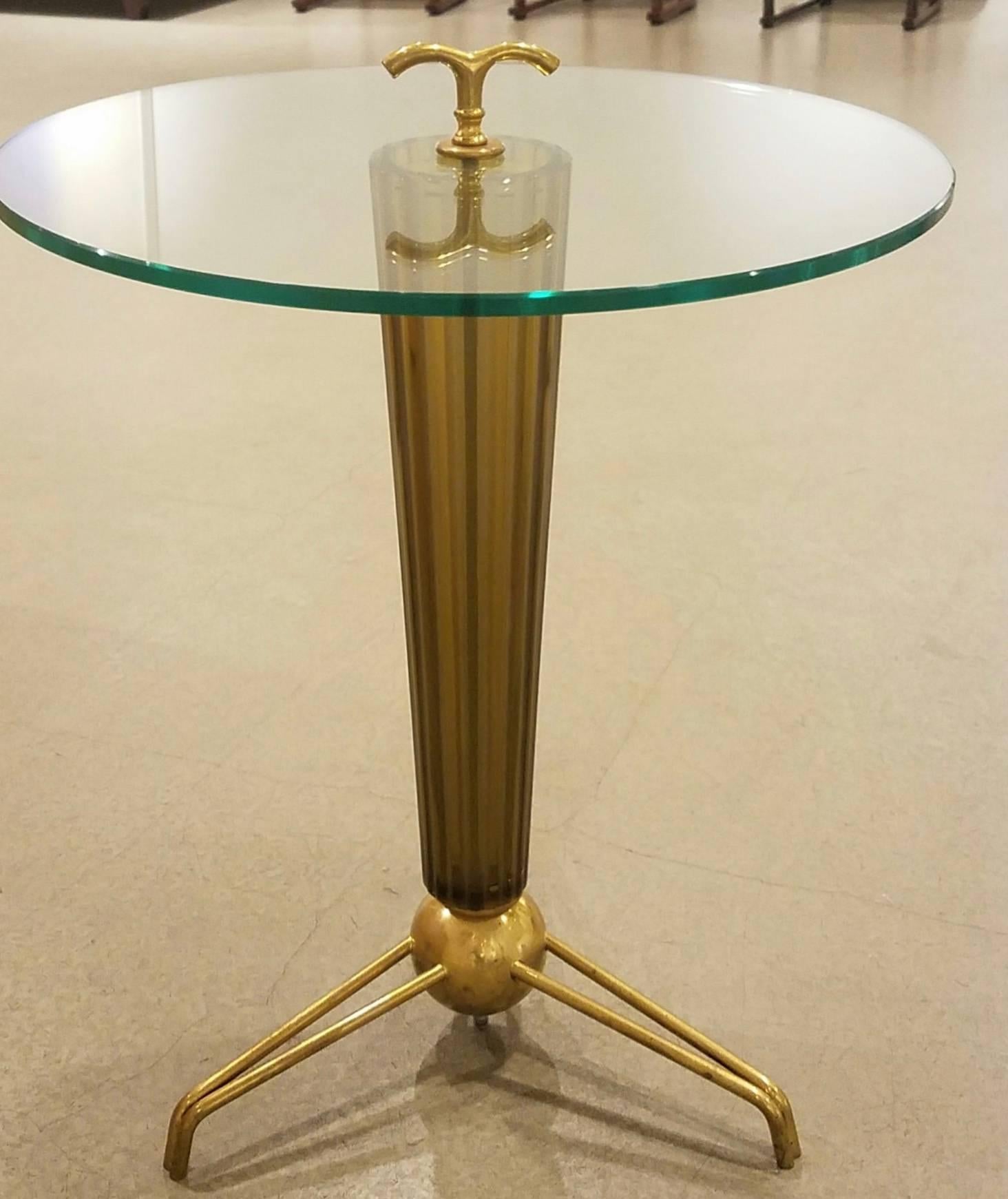 An Italian Mid-Century circular table with a clear glass top surmounted by a shaped brass finial supported by a thick conical, fluted, handblown Murano amber/bronze toned glass base capped by a large brass ball resting on a brass tripod base.