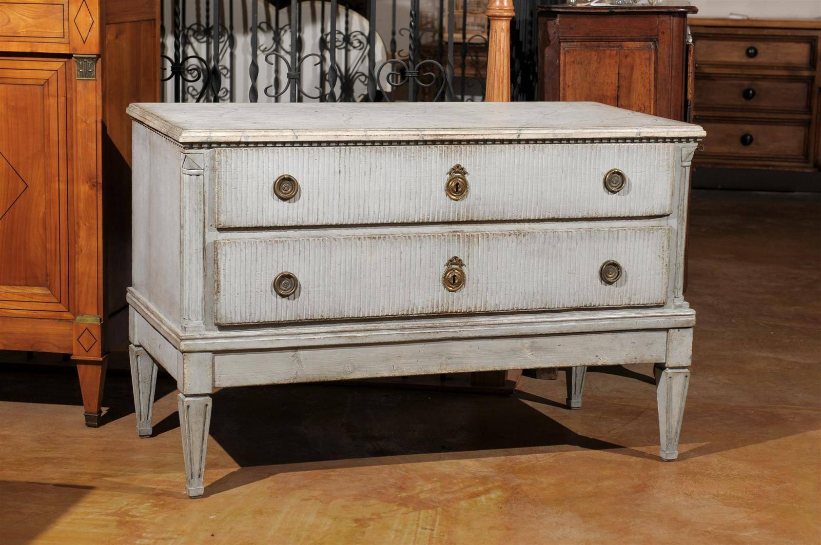 A Swedish period Gustavian painted wood two-drawer commode with reeded motifs and tapered legs from the late 18th century. This exquisite Swedish chest features a rectangular marbleized top with molded edges, sitting above a discreet dentil molding