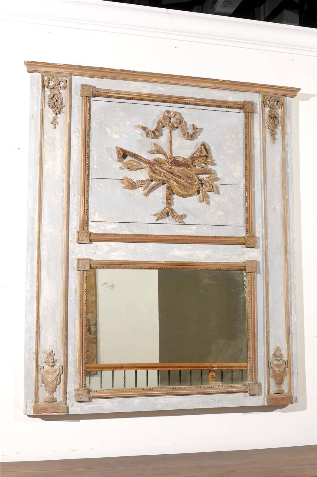 A French Neoclassical Revival painted and gilded trumeau mirror with ribbon-tied musical trophy and urns from the late 19th century. This French mirror was born in the later years of the 19th century, at a time when Neoclassicism, that had spread