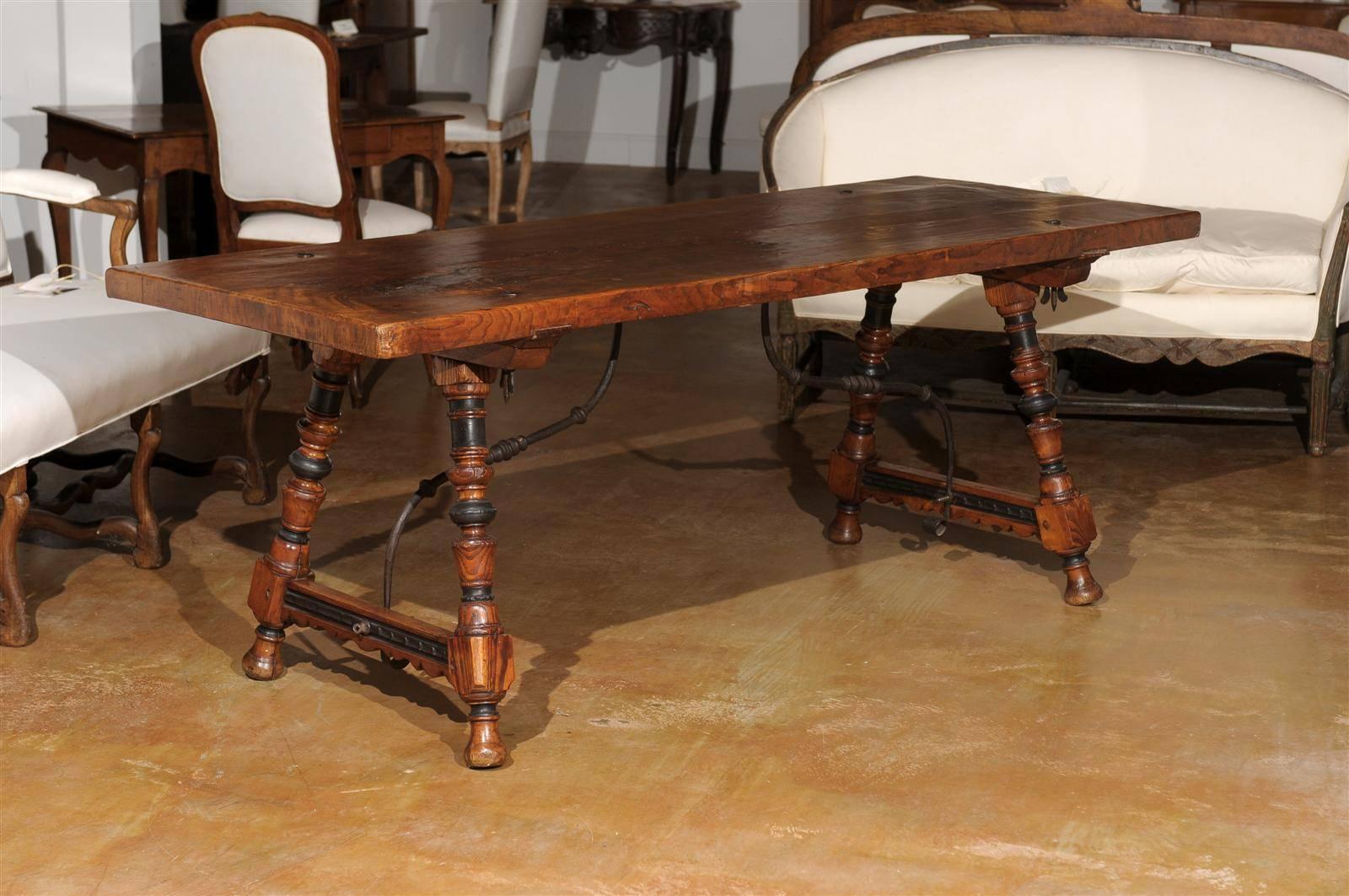 A Spanish Fratino dining table with hand made wrought-iron stretcher from the late 18th century. This Spanish wooden table features a sturdy rectangular top with iron nailheads sitting above an exquisite base made of splayed turned legs connected to