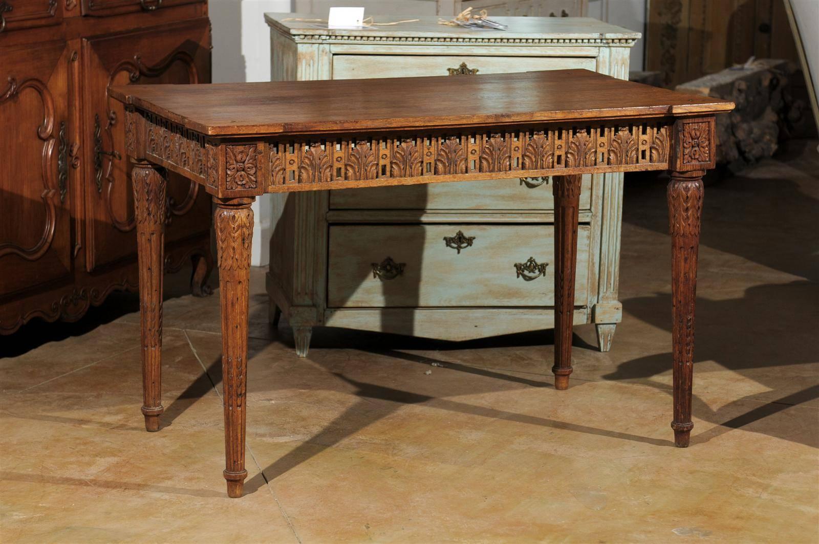 A French period Directoire carved oak side table with pierced apron on all sides from the early 19th century. This exquisite French table features a rectangular top with protruding corners, sitting above a striking apron, richly carved with palmette
