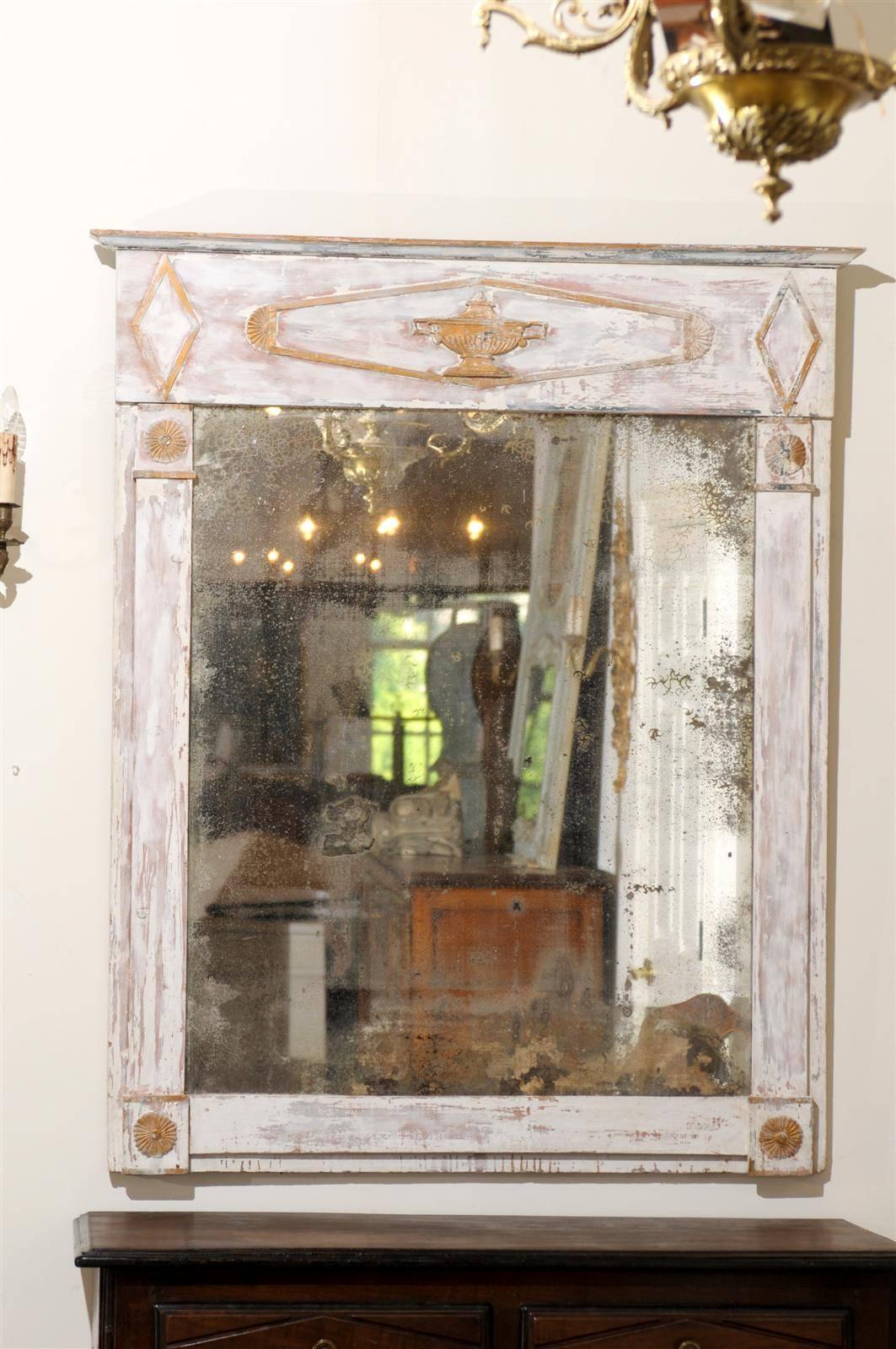 A French period Directoire trumeau mirror from the late 18th century with gilded accents, carved urn, distressed paint and mirror. This French Directoire mirror features an elegant linear Silhouette. The light colored distressed paint finish is