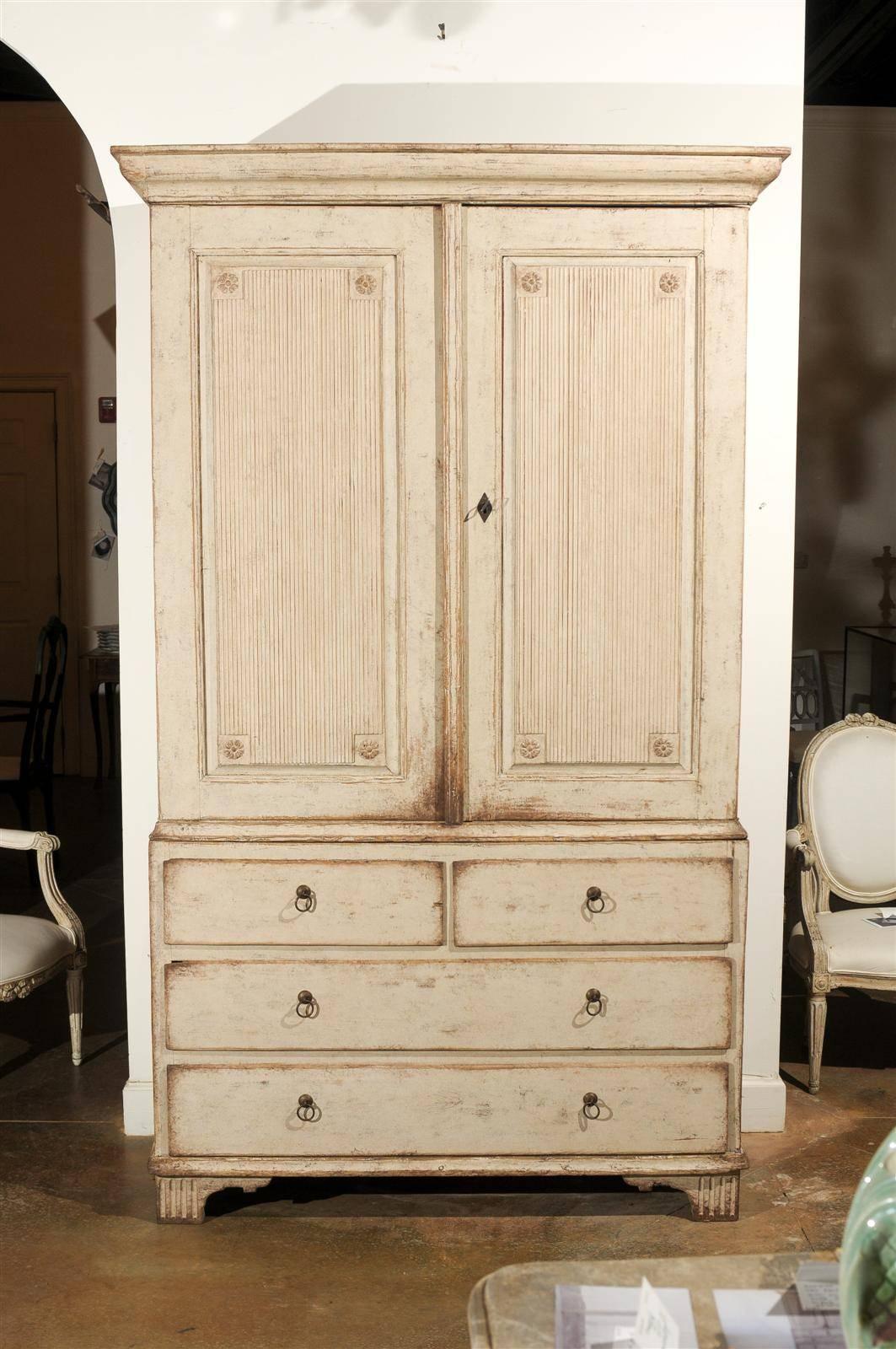 A Swedish Gustavian style painted wood two-part linen press with two doors in the upper cabinet over four drawers from the mid 19th century. This Swedish painted wood cabinet features a large molded cornice sitting above two tall reeded doors