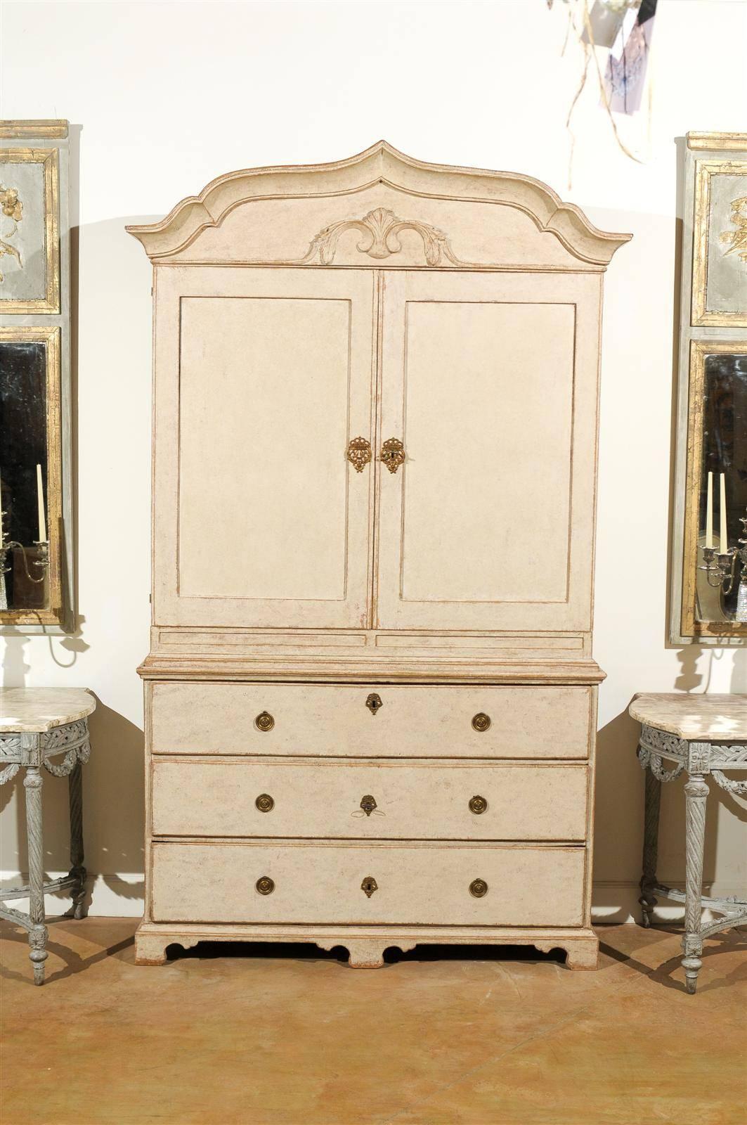 A Swedish Period Rococo painted wood cabinet with carved pediment, two doors over three drawers and original hardware from the mid 18th century. This exquisite Swedish linen press features a cross-bow shaped molded pediment, proudly sitting above an