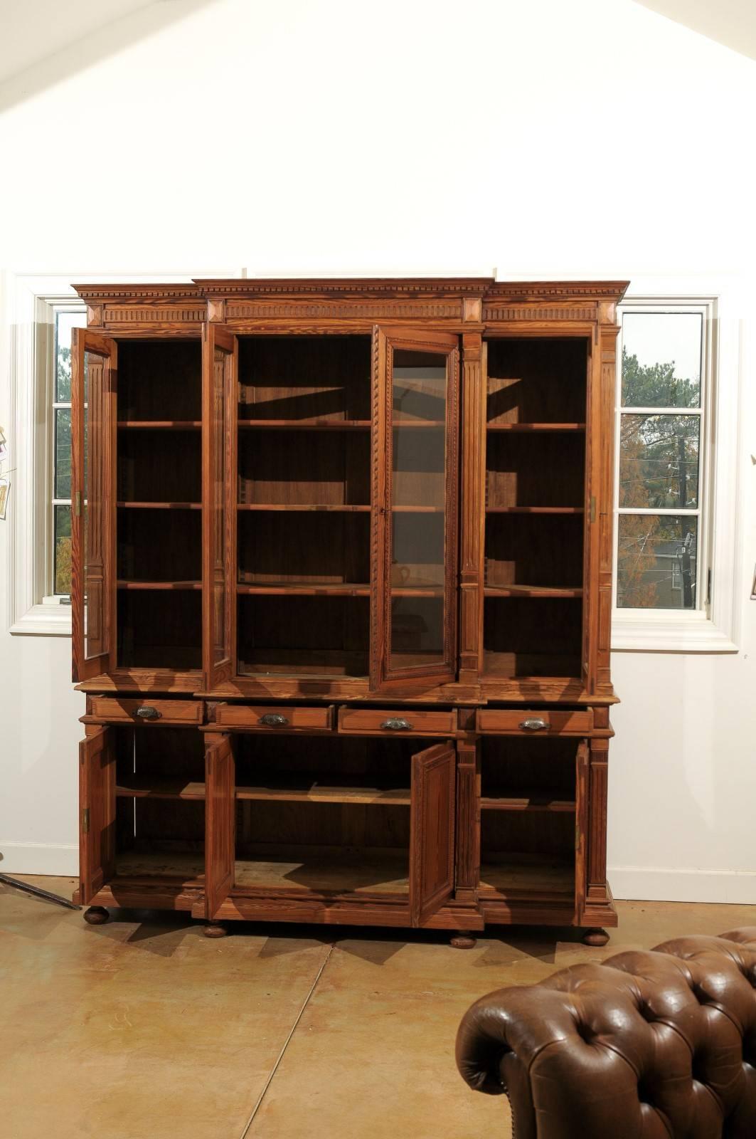 A French pitch pine and glass door breakfront bookcase from the turn of the century. This French bookcase features four glass doors making up the upper part of the piece. The bookcase is adorned with a dentil molding on the upper cornice,