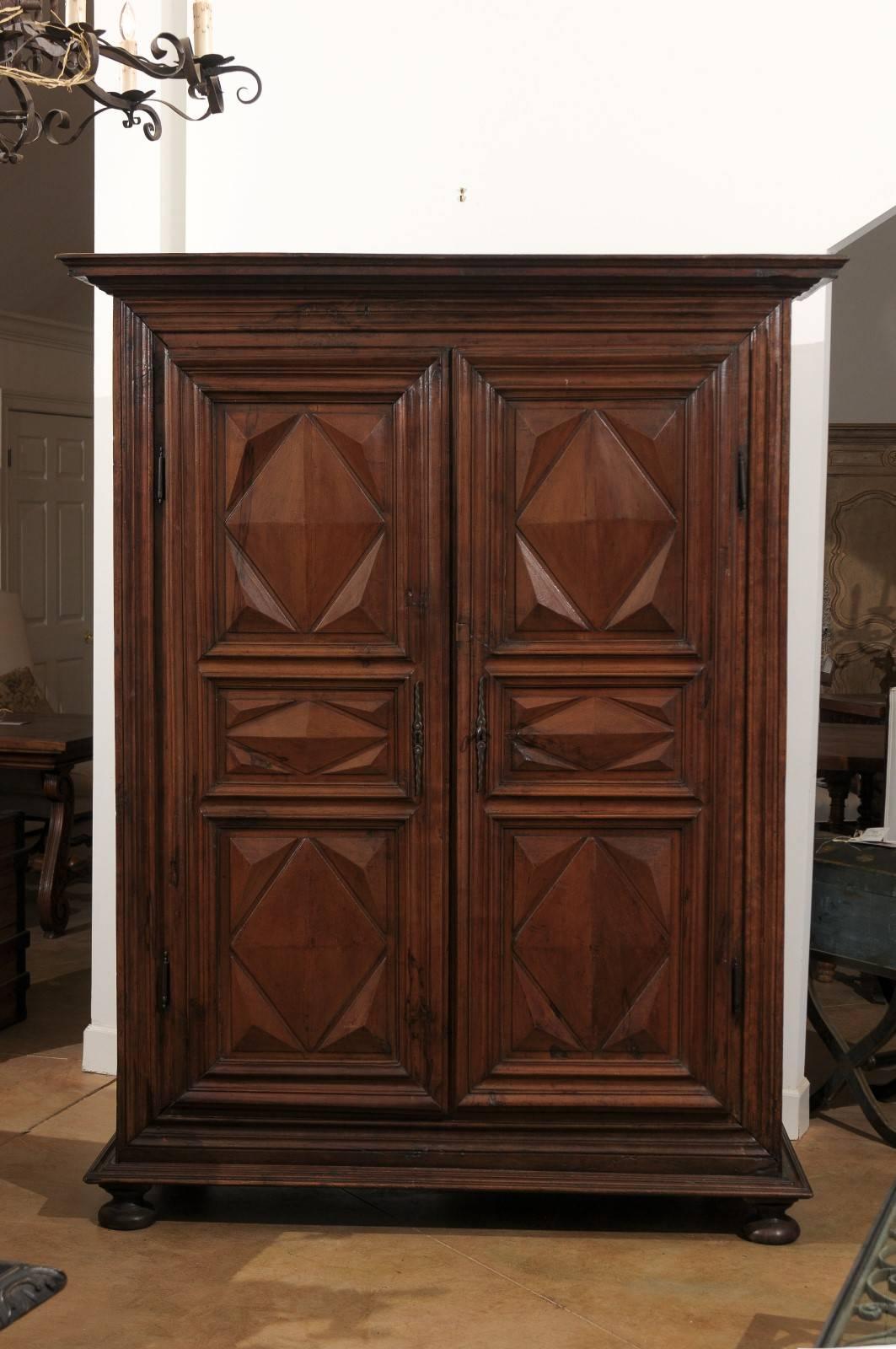 A mid 17th century French Louis XIII period walnut armoire with diamond-shaped motifs and bun feet. This French carved wood armoire features a large molded cornice, sitting above two beautifully carved doors adorned with diamond-cut motifs (pointes