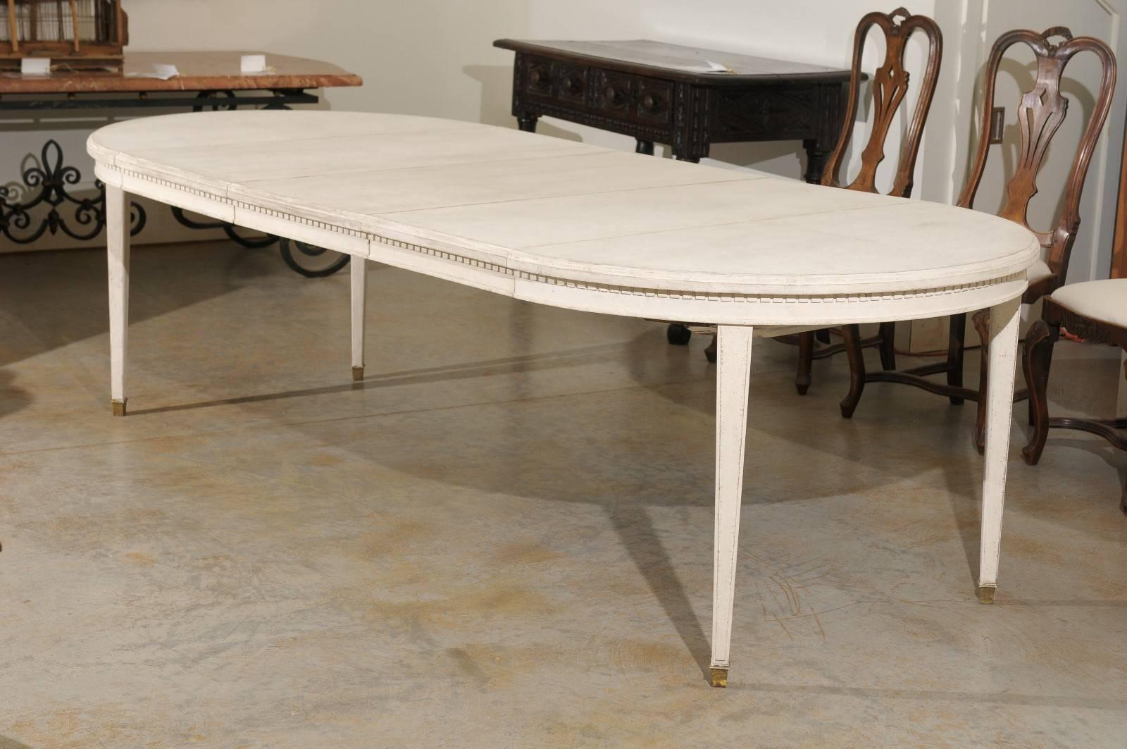 A Swedish Gustavian style painted dining room table with extensions from the early 20th century. This Swedish dining room table circa 1900-1920 features a circular top discreetly adorned with a dentil molding on the apron. Raised on four slightly