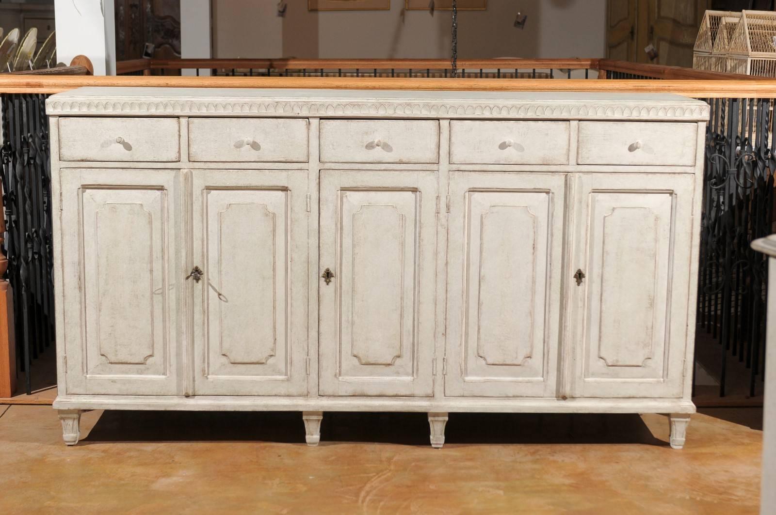 A Swedish painted wood five-door and five-drawer enfilade from the late 19th century. This Swedish long buffet features a rectangular top adorned with a carved molding on three sides. The motifs evoke the simplicity of broken arches of an early