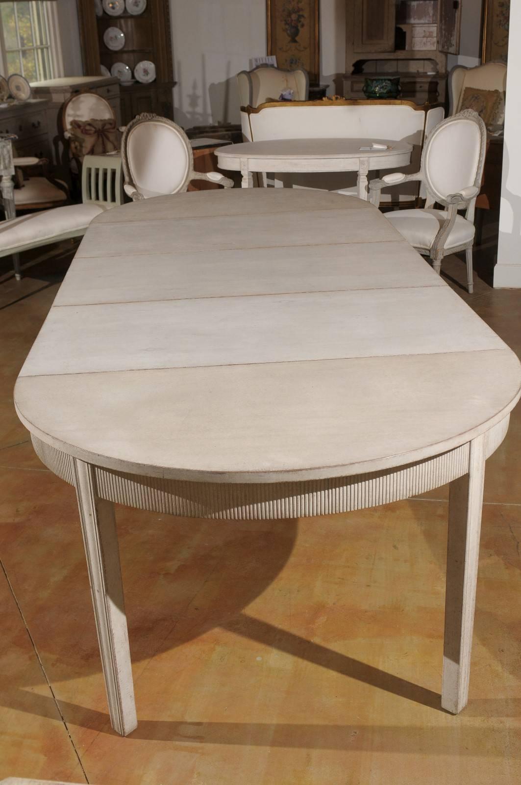A Swedish Gustavian style painted wood extension dining room table from the late 19th century with carved apron and three leaves. This Swedish dining room table features the clean silhouette typical of the Gustavian style. Without its additional