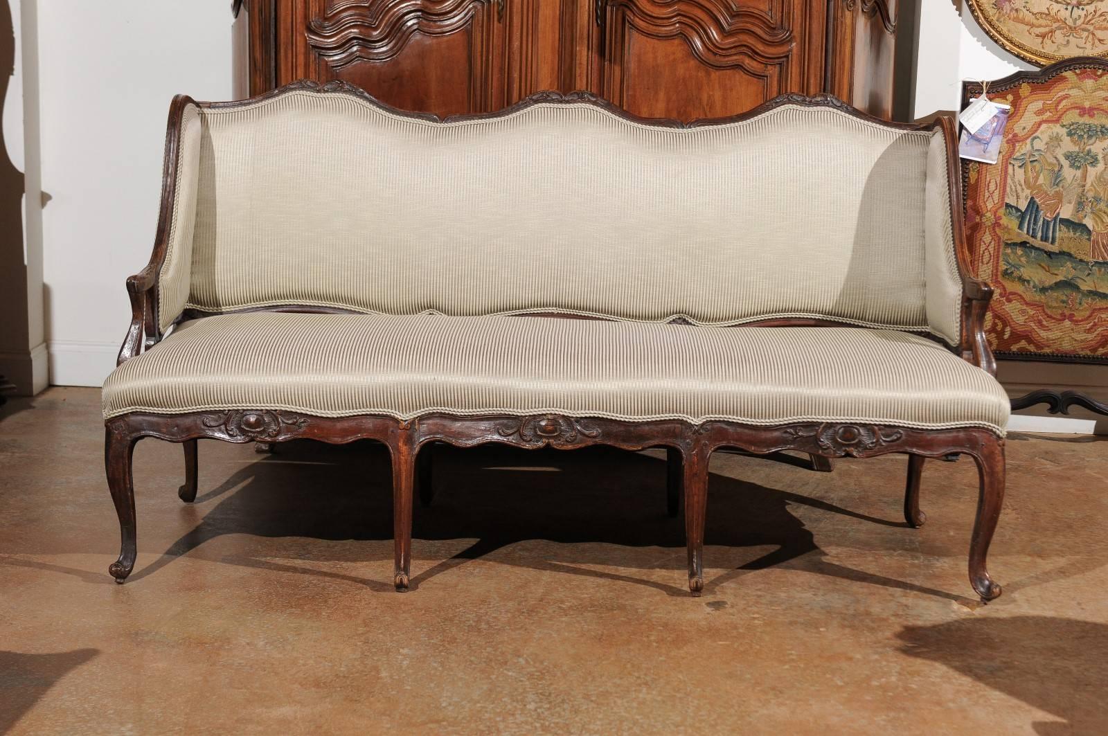 A French Régence period walnut three-seat canapé à oreilles from the early 18th century with carved skirt and new upholstery. This French canapé was born during the short years of the Régence that saw the transition of power between feu King Louis