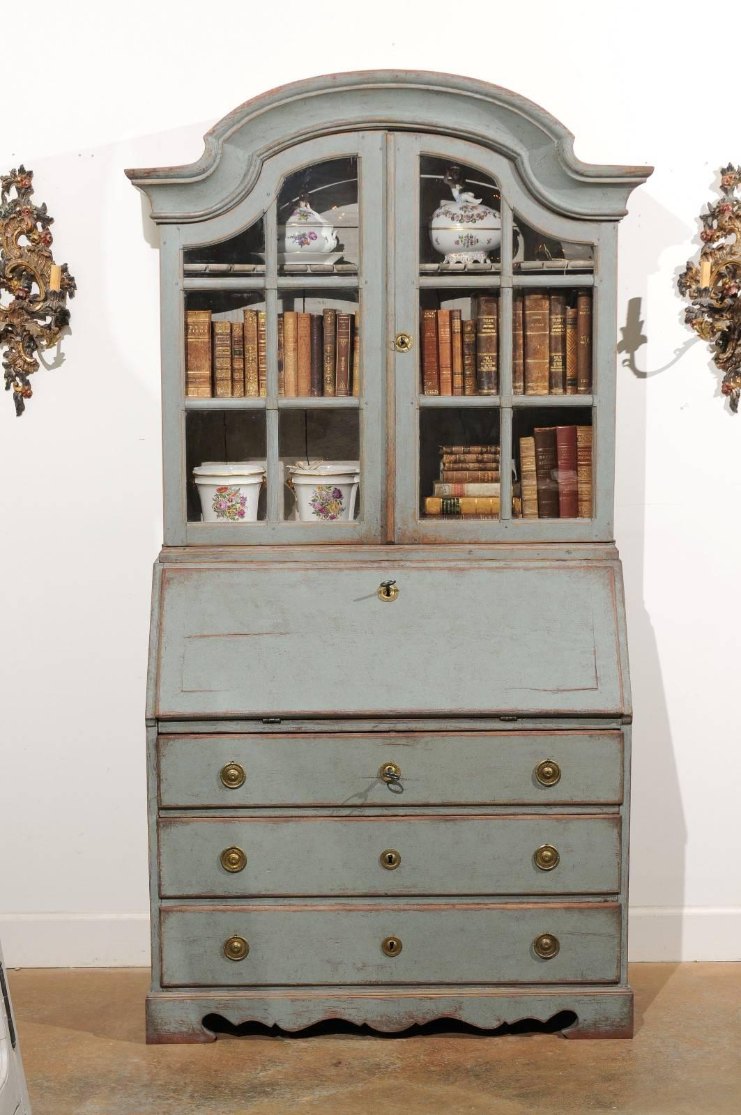 A Swedish Rococo style light grey / blue painted tall secretary with glass doors cabinet from the late 19th century. This Swedish secretary features a bonnet shaped pediment sitting atop two panelled glass doors. These doors open to reveal inner