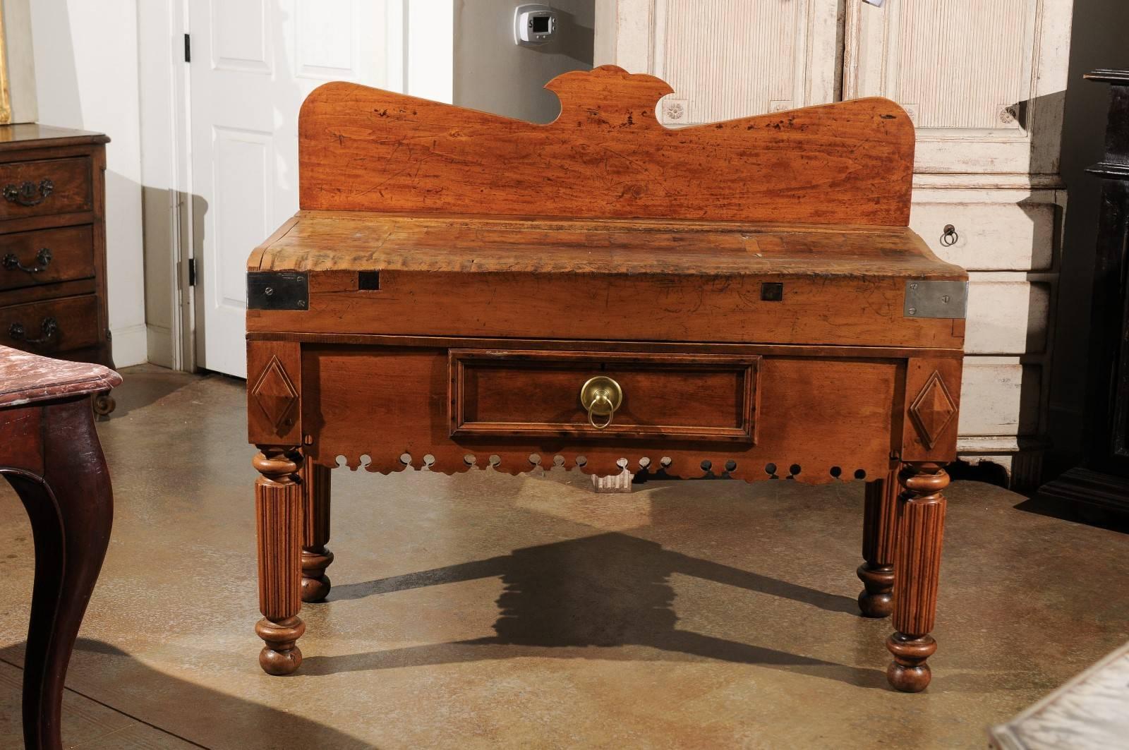 This French rectangular butcher block table from the early 19th century features a beautiful back with a carved motif in the centre of its crest. The table is raised on four fluted legs resting on ball feet. The nicely scalloped apron on three sides