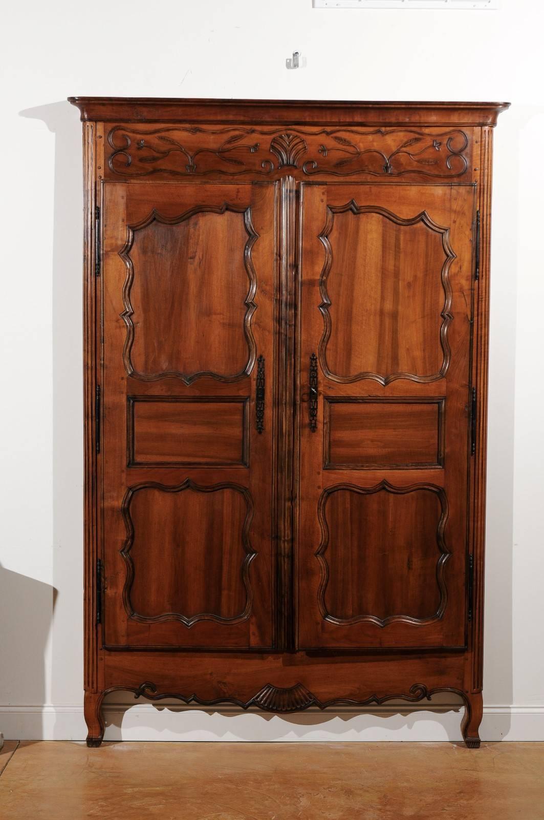 This French Louis XV style walnut armoire façade from the mid-19th century features double pegged doors with harmoniously carved panels, topped with a cornice and delicate floral-shaped ornaments, and flanked with fluted side posts. The rectangular