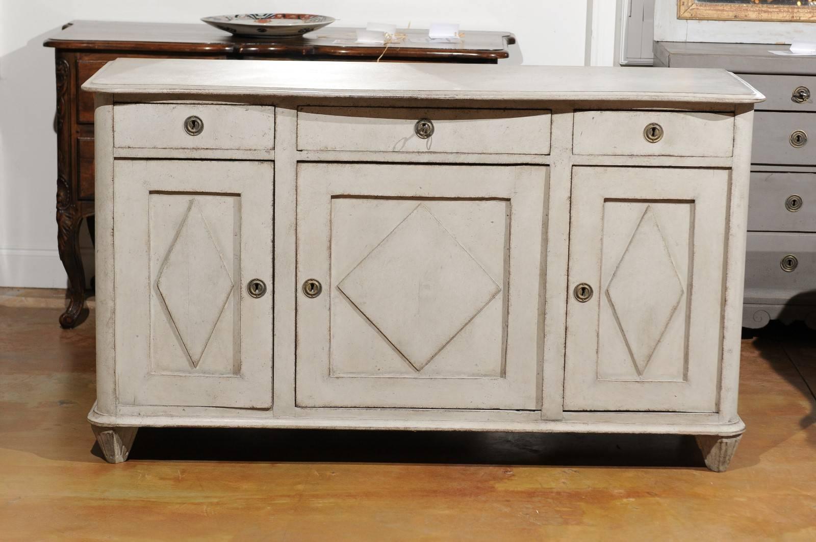 A Swedish Gustavian Style painted wood enfilade with three drawers over three doors from the mid-19th century. This Swedish long enfilade features a serpentine top sitting above three drawers and three doors. Each door is beautifully adorned with a