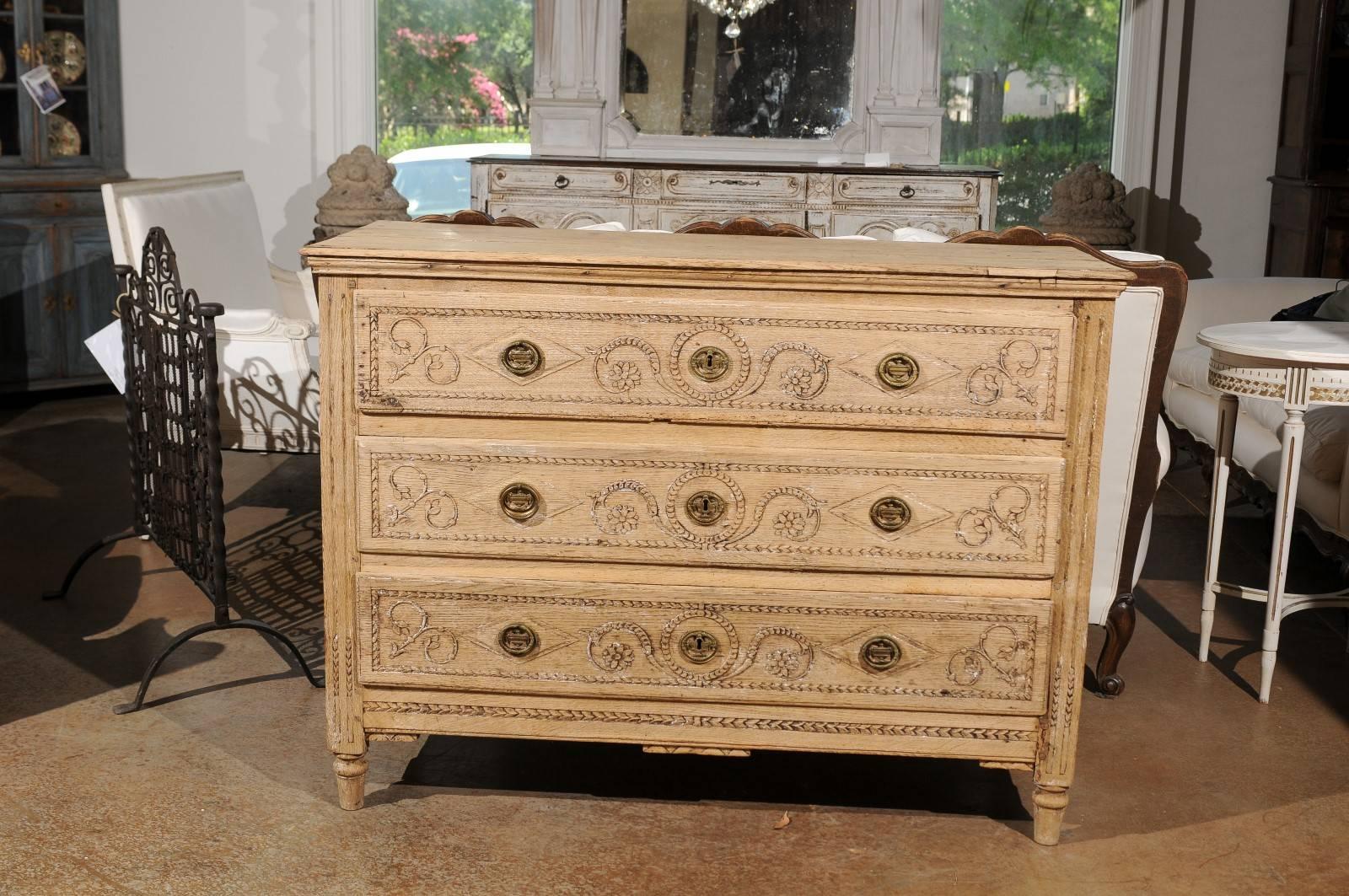 A French 18th century Louis XVI three-drawer bleached oak commode with rinceaux motifs. This French commode features a rectangular three-plank top with bevelled edge over three carved drawers. Each drawer, grooved on the side to receive the runner,