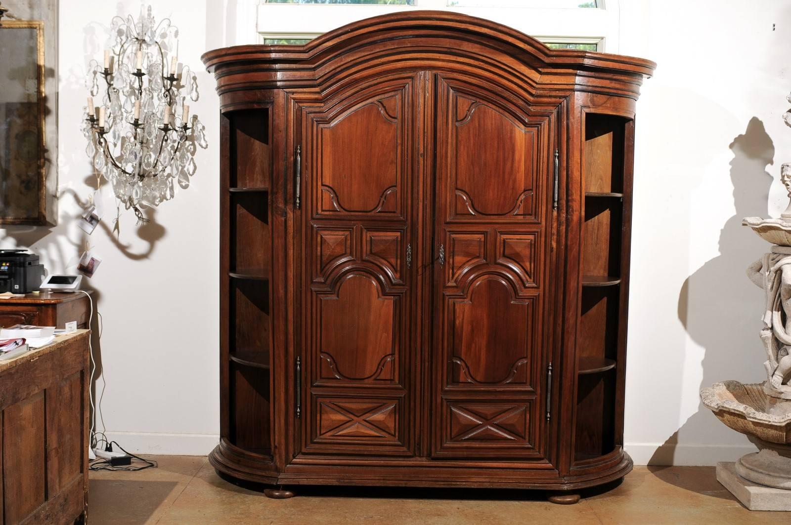 A French Louis XIII style walnut armoire with bonnet-shaped pediment, curved open side shelves, geometric motifs and original hardware from the early 19th century. This French armoire was born in the second decade of the 19th century, in an ever