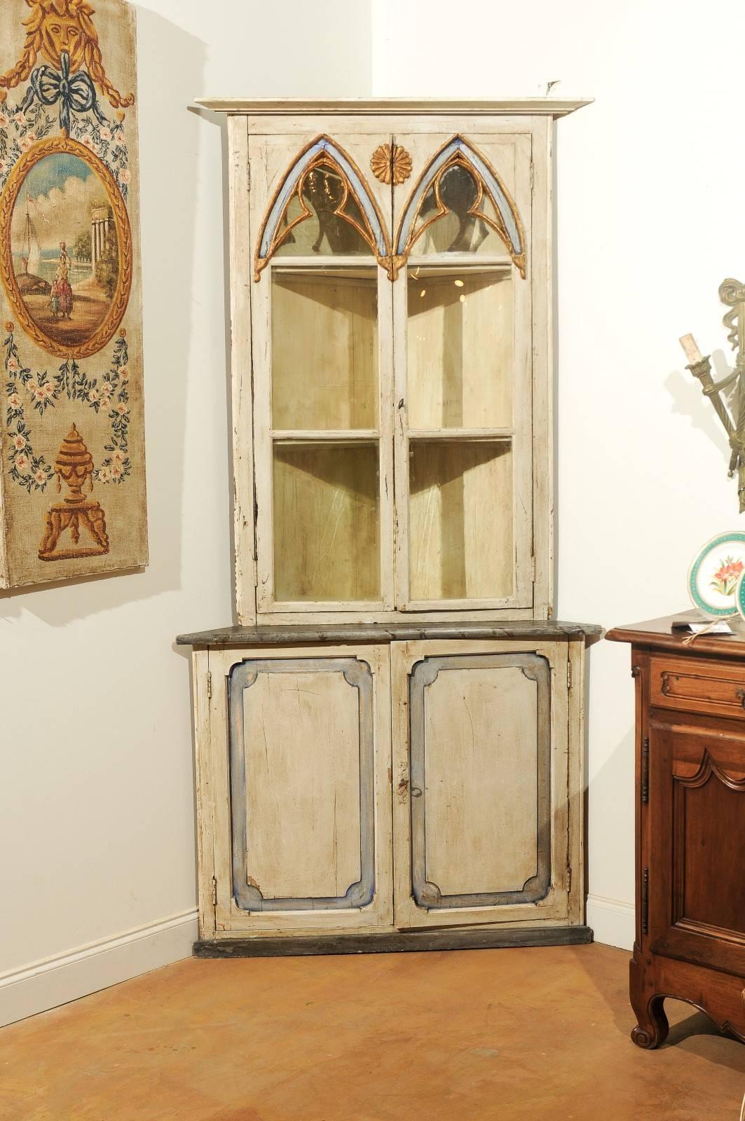 A Swedish Gothic Revival painted wood and glass doors corner cabinet from the mid-19th century. This exquisite Swedish corner cabinet features a molded cornice overhanging two Gothic inspired doors with glass panels. A giltwood rosette, carved onto