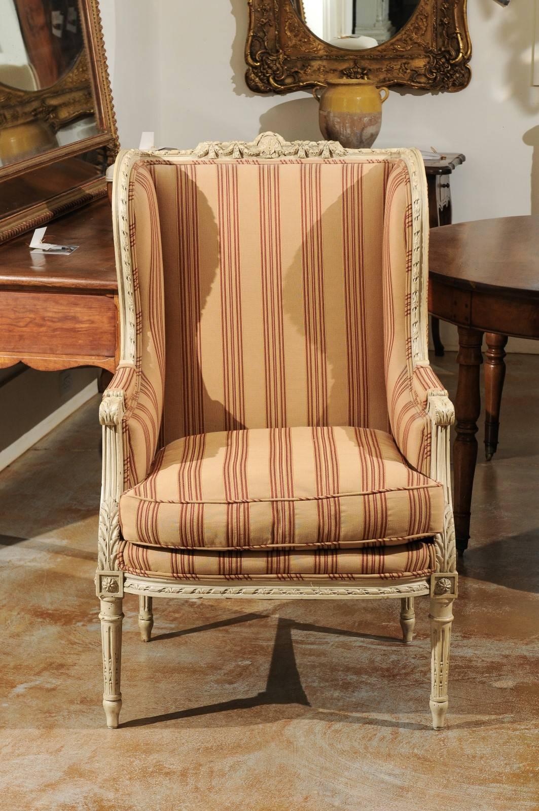 This French Louis XVI style wingback painted wood chair from the late 19th century features a beautifully carved crest on the top rail, adorned with a central rosette flanked with swags tied to delicate ribbons. This 