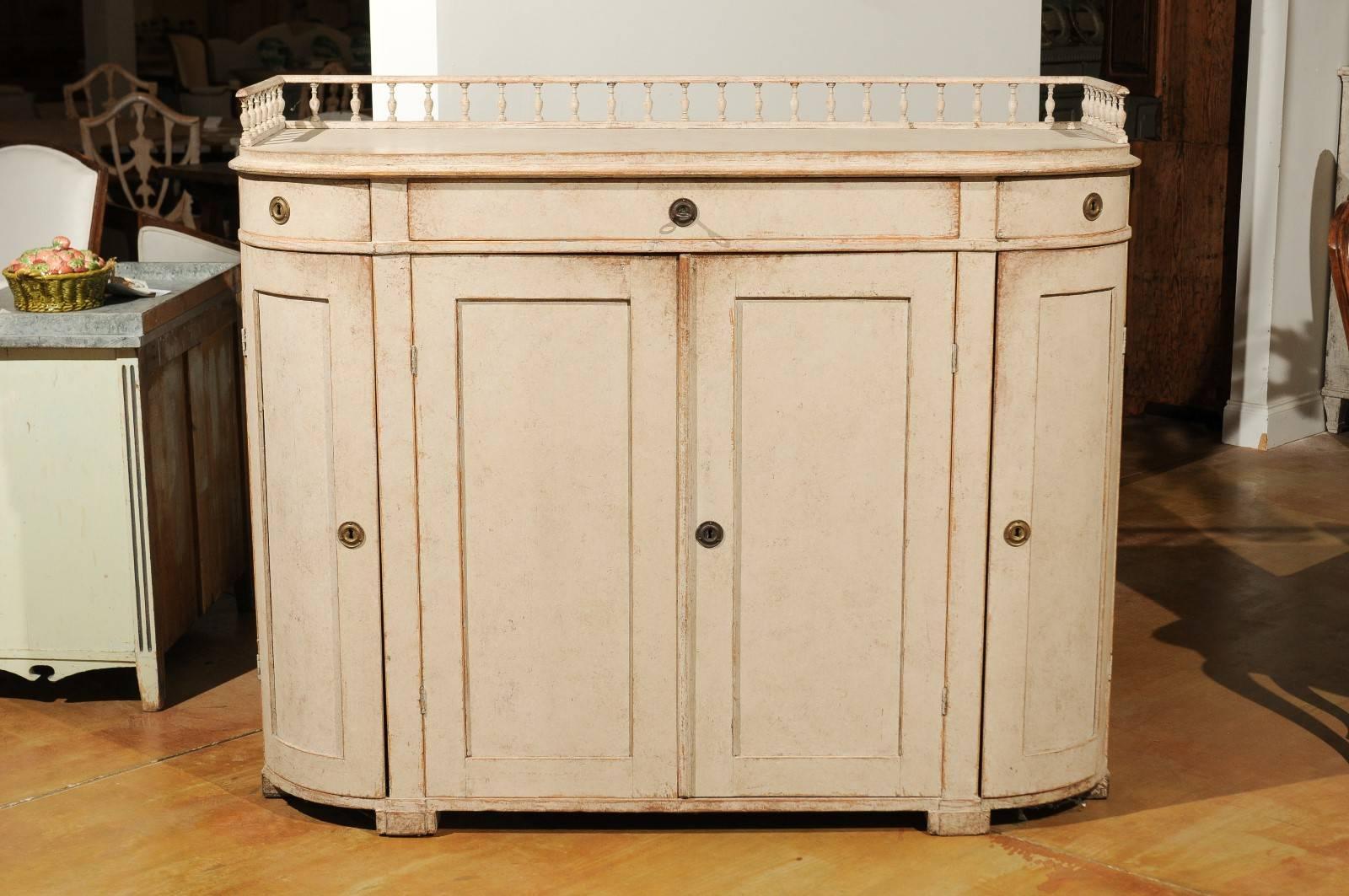A Swedish Karl Johan style wooden painted demilune sideboard with three-quarter baluster gallery and three drawers over three doors from the late 19th century. This Swedish sideboard or demilune cabinet features a delicate balustrade gallery on the