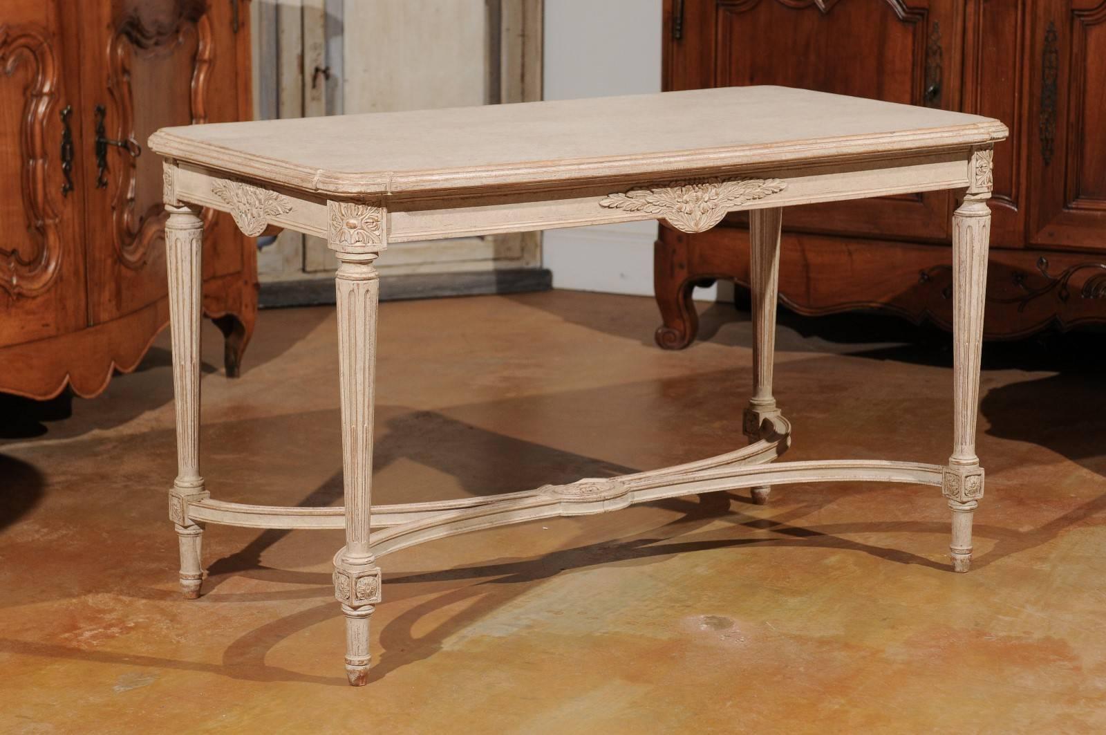 A Swedish Gustavian style painted wood coffee table with fluted legs and cross stretcher from the early 20th century. This Swedish coffee table features a rectangular top with beveled edges and rounded corners, sitting above an exquisitely carved