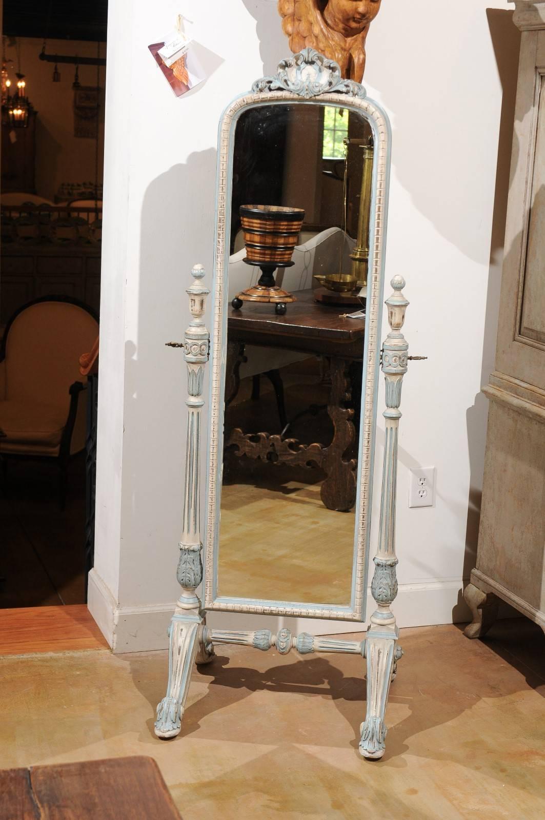 An Italian painted wood freestanding cheval mirror from the early 20th century. This Italian mirror features a delicately carved body, painted in a soft cream palette with light blue accents. The mirror, reminiscent of an elongated Louis-Philippe,