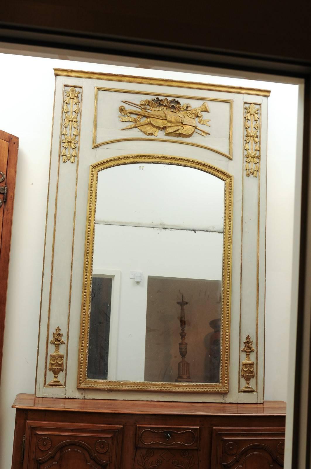A French Louis XVI period 18th century painted and gilt trumeau mirror with evocation of the arts and original glass. This French Louis XVI large trumeau mirror features a light grey painted linear frame, highlighted with giltwood accents. Our eye