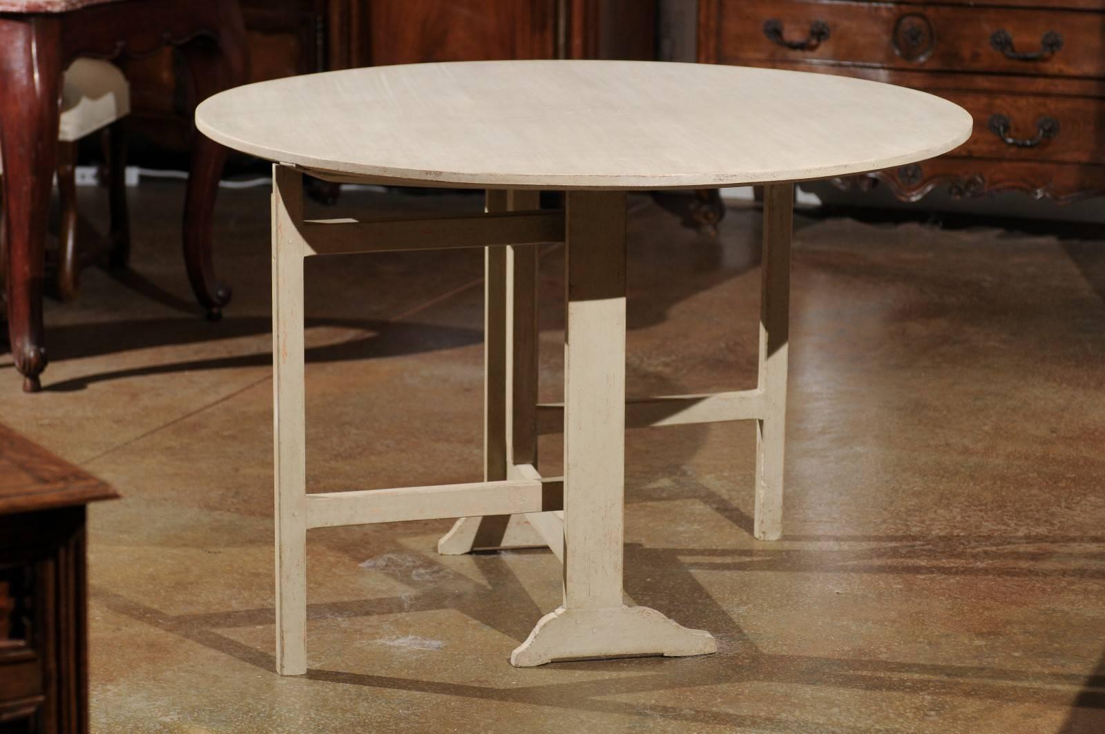 A Swedish painted round wine tasting gateleg table from the late 19th century. This Swedish centre table, circa 1890 features a circular top over an H-form trestle base with gateleg support. Painted in a light color, the table, with its Scandinavian
