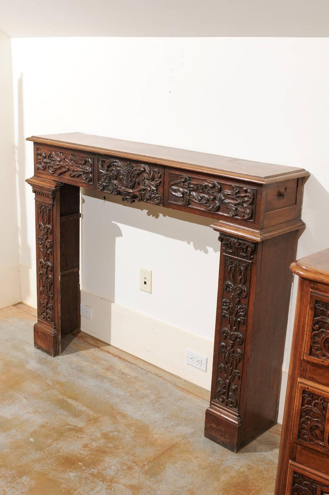 A French Renaissance Revival carved wood fireplace mantel with drawers from the late 19th century. This French fireplace mantel features a richly carved surround, showing us the renewed taste for classical styles of the 1880s. A central drawer is