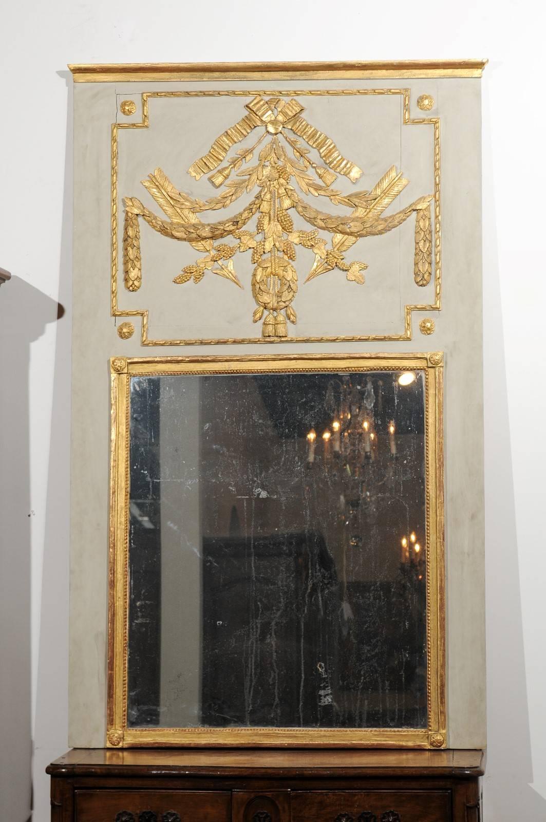 A French 18th century Louis XVI period painted and gilded trumeau mirror with carved motifs. This French trumeau features a linear light grey green painted frame, beautifully accented with a profusion of gilded motifs. In a manner typical of