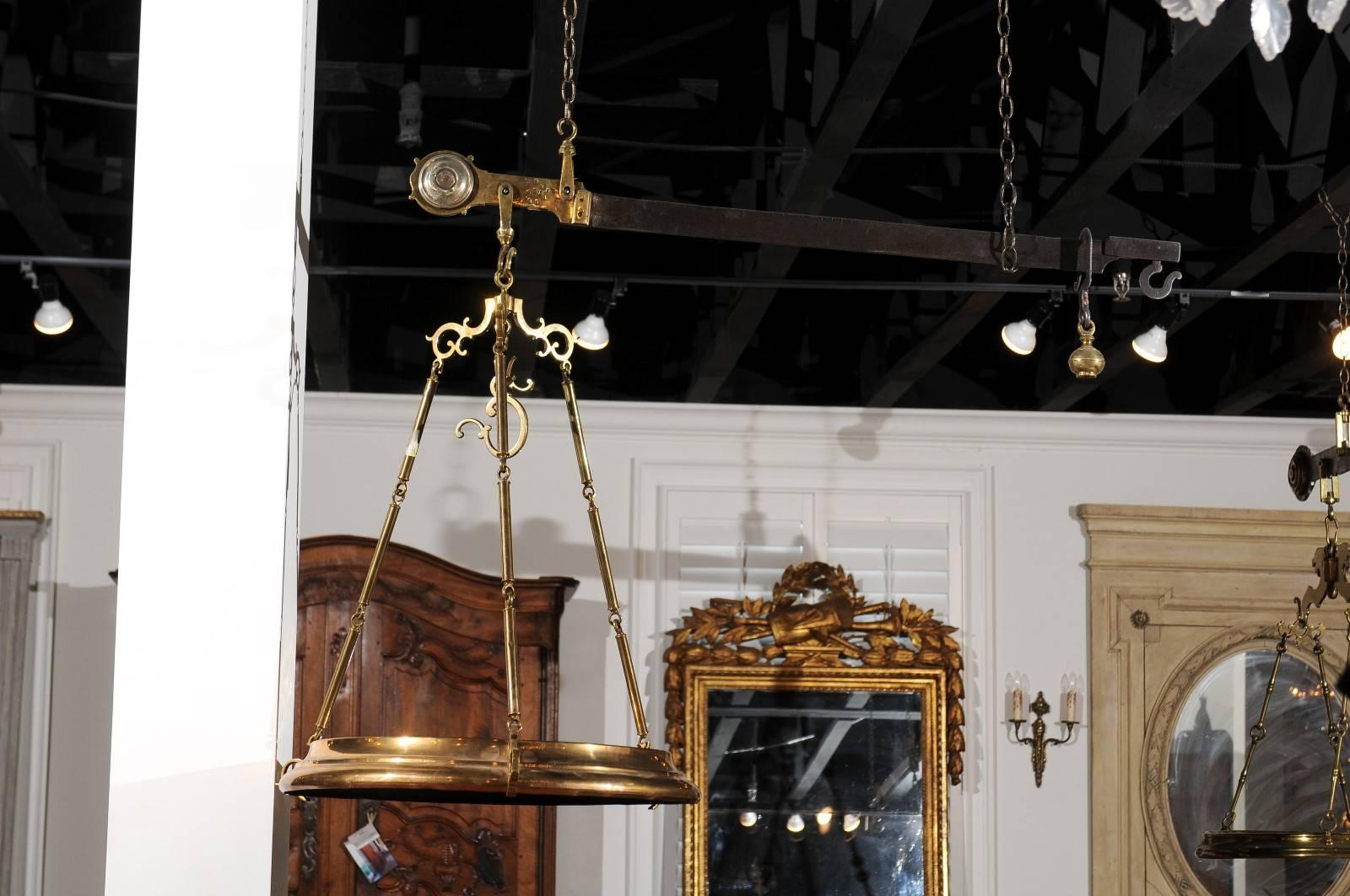 A French brass hanging butcher's scale from the 19th century. This French scale features a horizontal beam with its weight at the end. A circular tray, connected to the top with three profiled links hangs below. The upper beam will hang from the