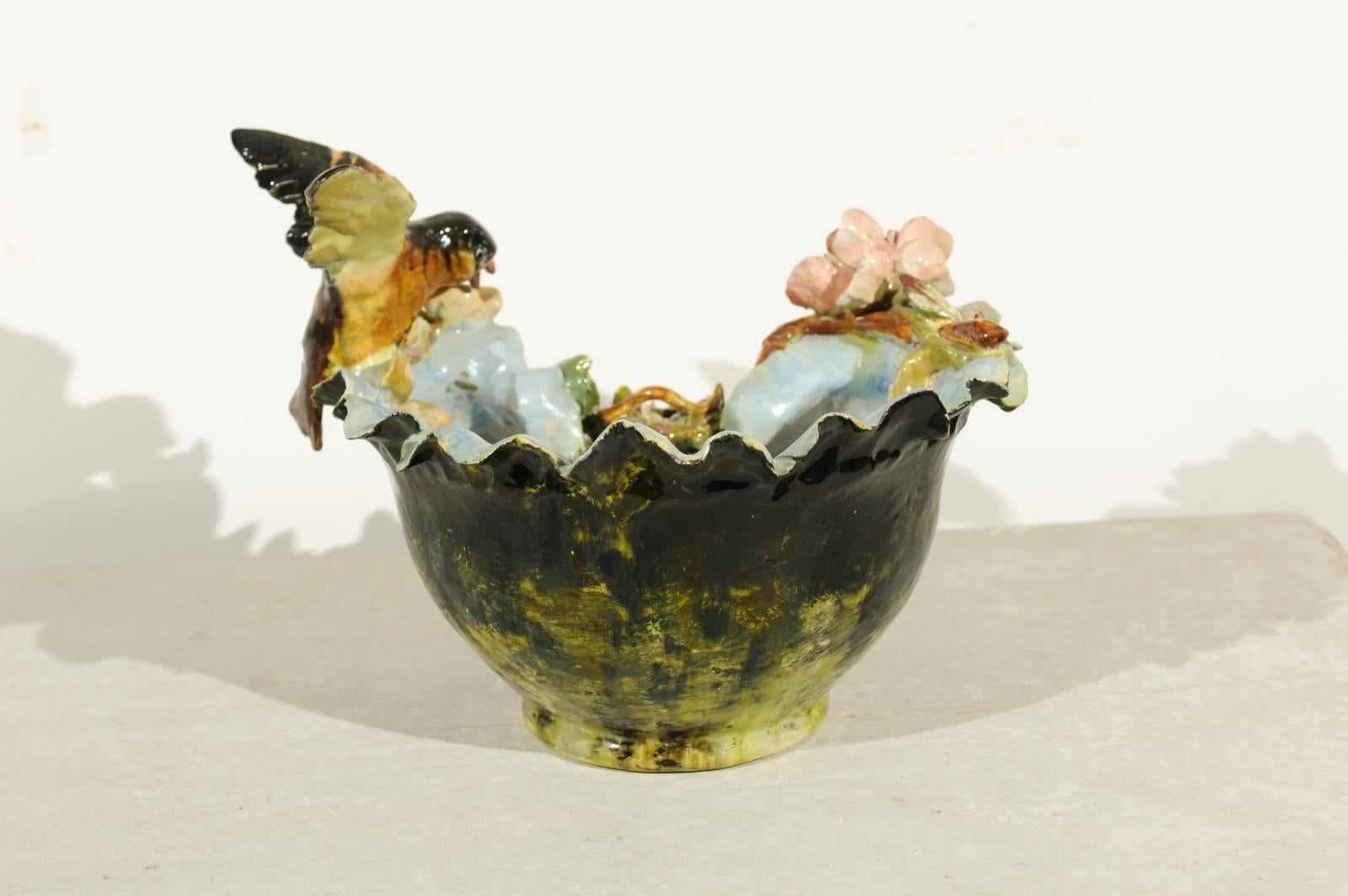 A 19th century petite French faience bowl adorned with a bird and bird nest barbotine décor. This French pottery features a green colored body, decorated with exquisite colorful flowers. A small bird just landed on the lip of the bowl, to check on