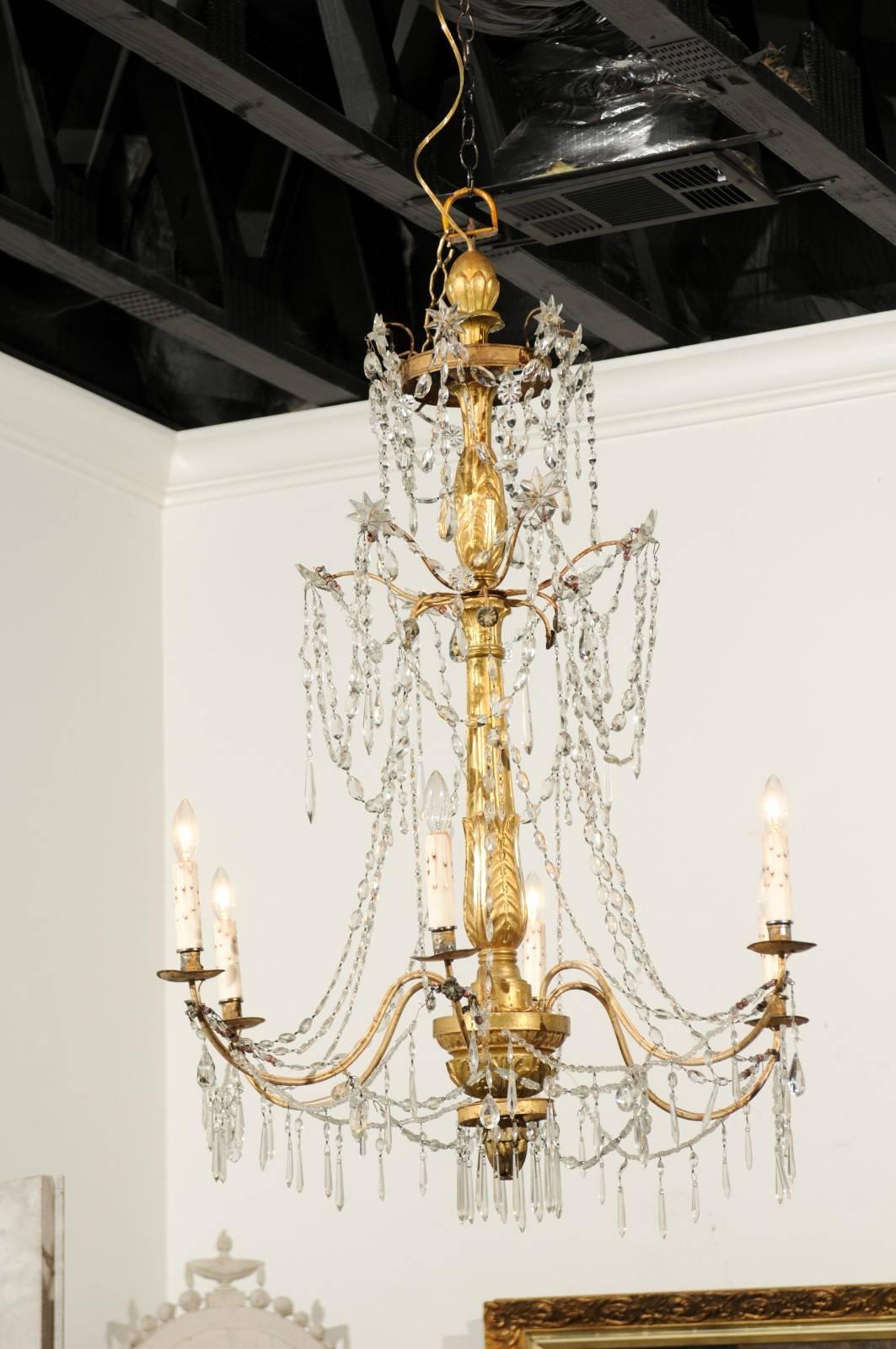 An Italian giltwood and crystal six-light chandelier from the mid-19th century. This Italian chandelier features a central giltwood staff, adorned on its surface with carved waterleaves and gadroons. Strands of faceted crystals accented with