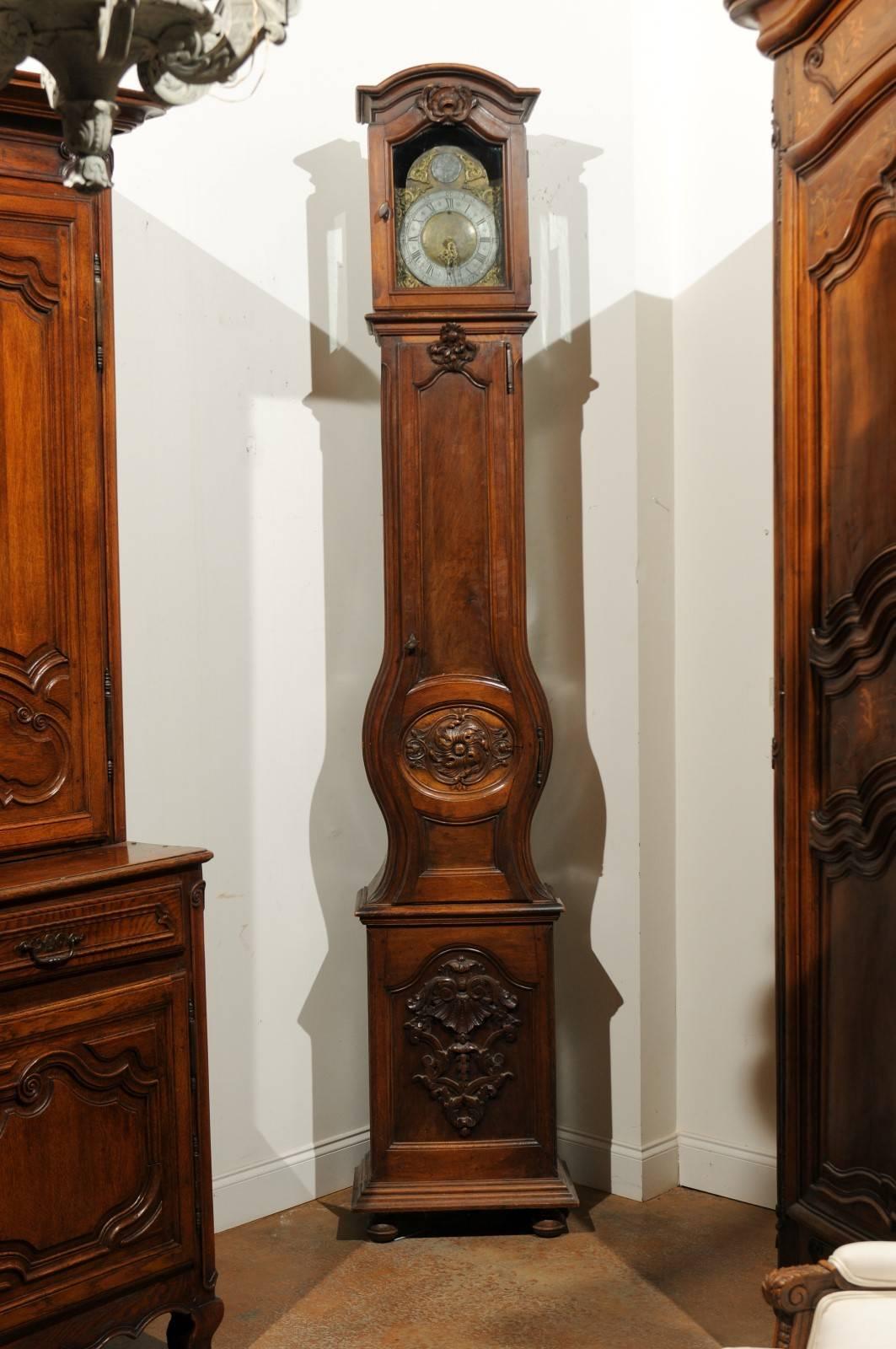 A French mid-18th century Louis XV period walnut longcase grandfather clock from the Rhône Valley. This French tall walnut clock features a rectangular head topped with a bonnet pediment surmounting a rocaille motif. The face is made of a