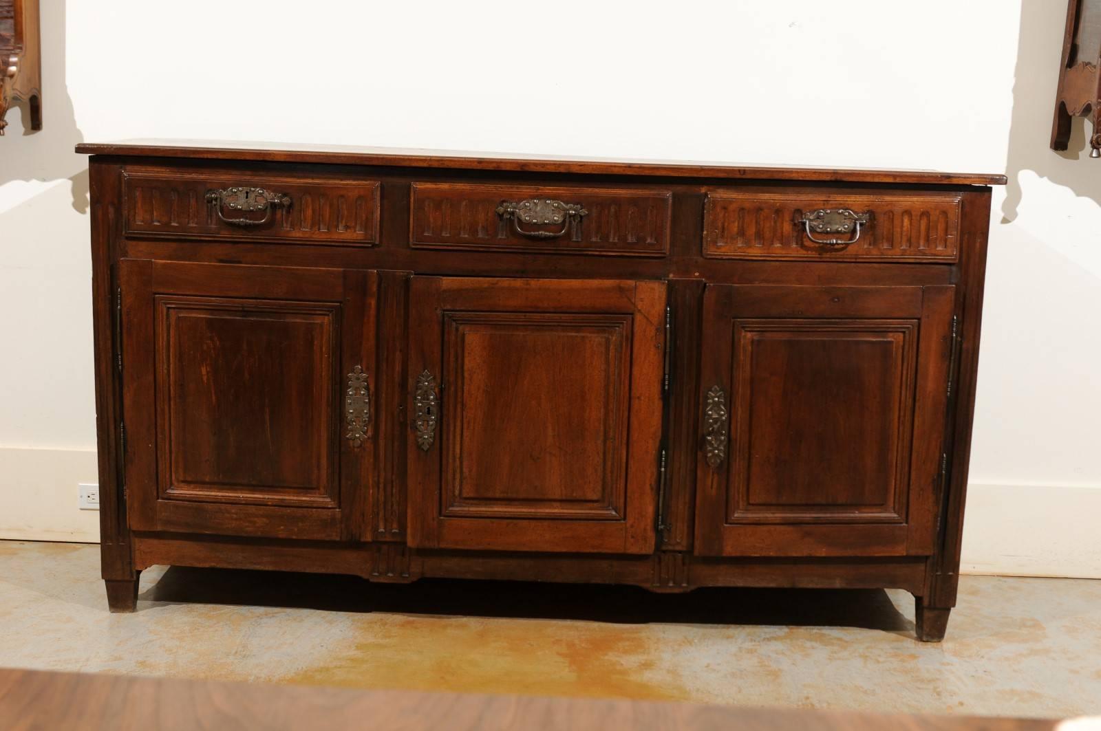 A French period Louis XVI walnut enfilade with three drawers over three doors from the late 18th century. This French long buffet features a rectangular top sitting above three hand-cut dovetailed drawers adorned with fluted patterns and exquisite