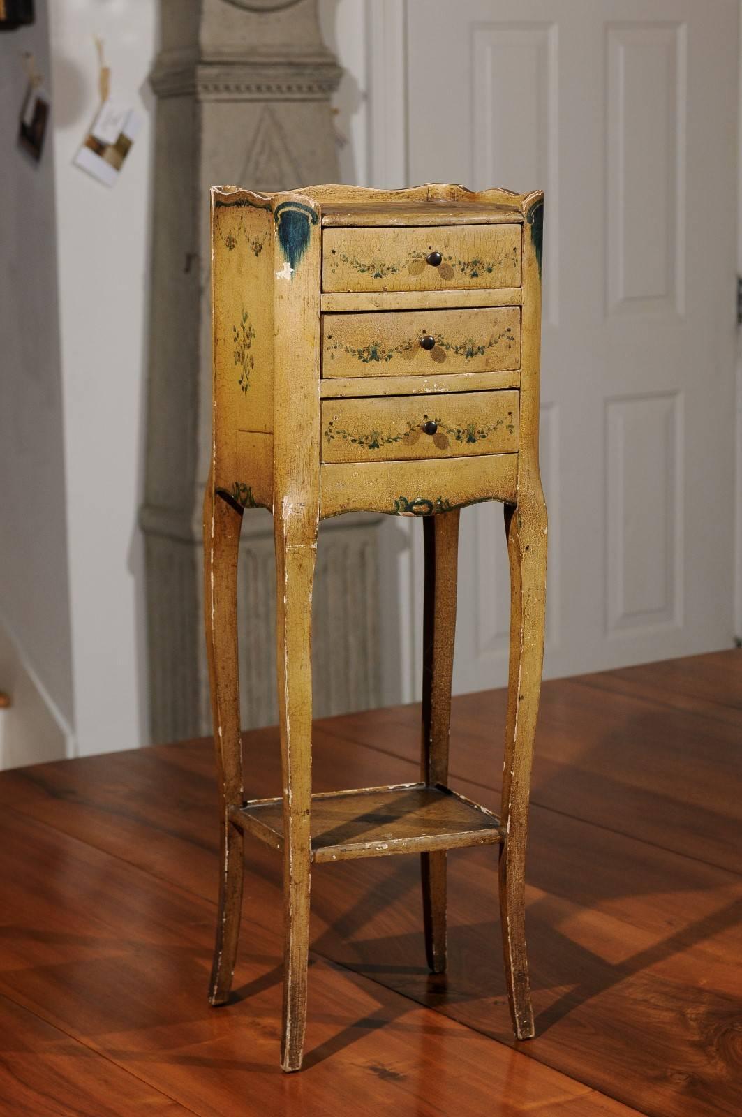 A 19th century Italian nightstand table with painted decor, three drawers and lower shelf. This Italian nightstand table features a rectangular top adorned with a charming painted scene, surrounded with a wooden three-quarter gallery. Three