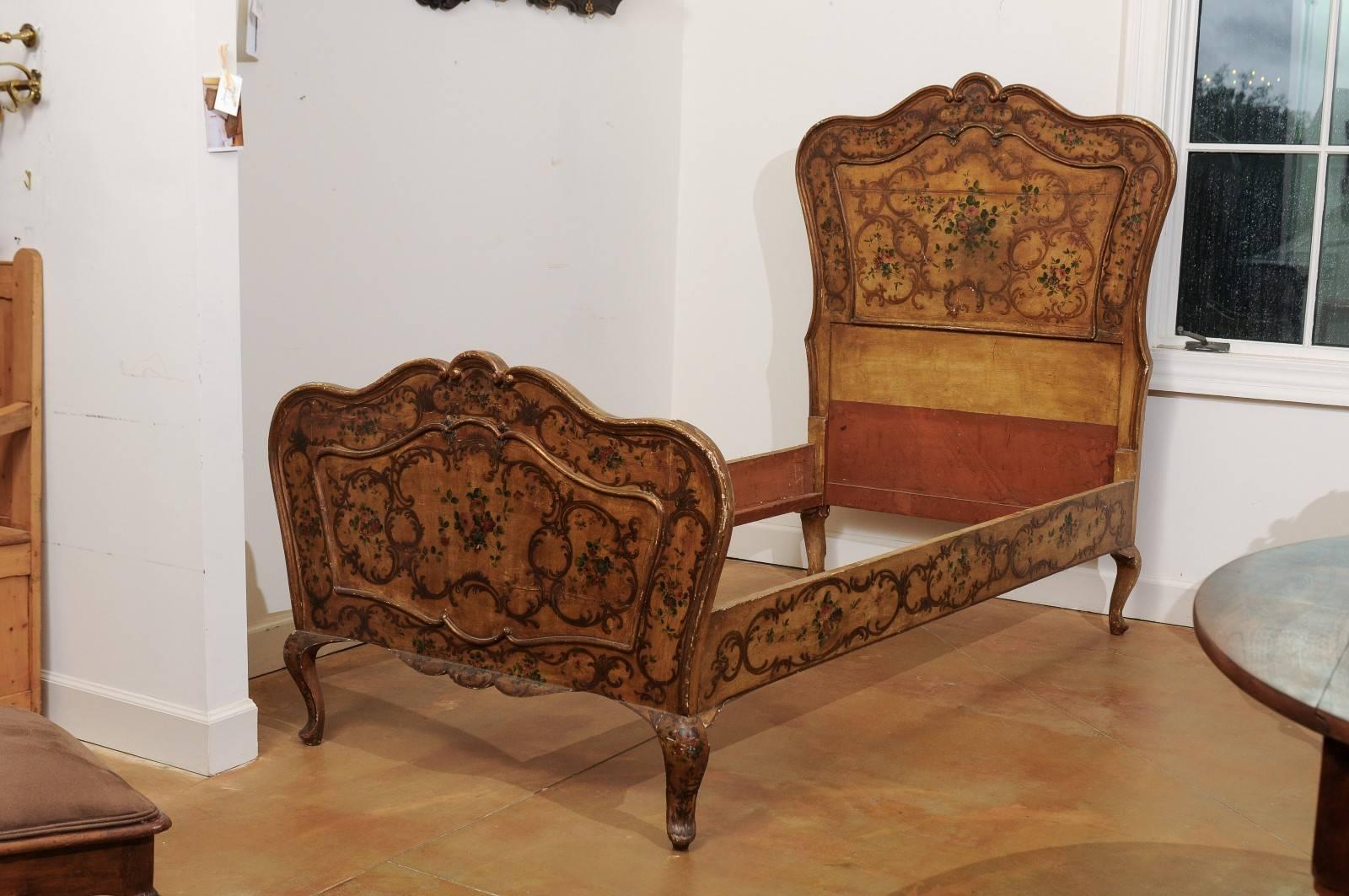 An Italian Rococo style twin XL bed frame with painted décor from the early 19th century. This Italian wooden bed frame features an exquisite curvy Silhouette, adorned with delicately arranged scrolls and floral motifs. The tan color is the perfect