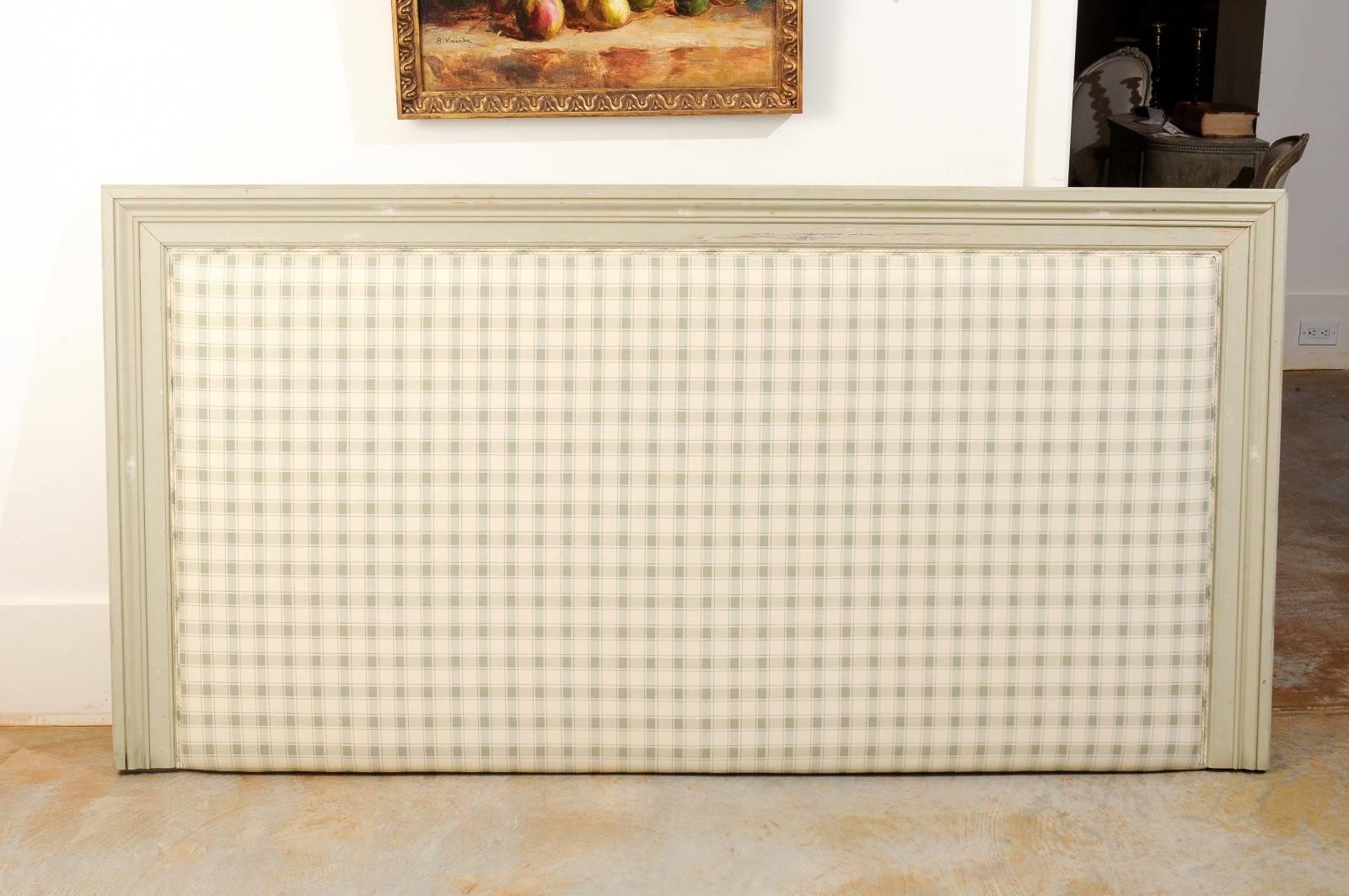 A king-size upholstered headboard made from a French antique door molding and covered in plaid fabric. This contemporary headboard features an antique French molded wooden door molding painted in a light color. The clean, simple lines of this wooden