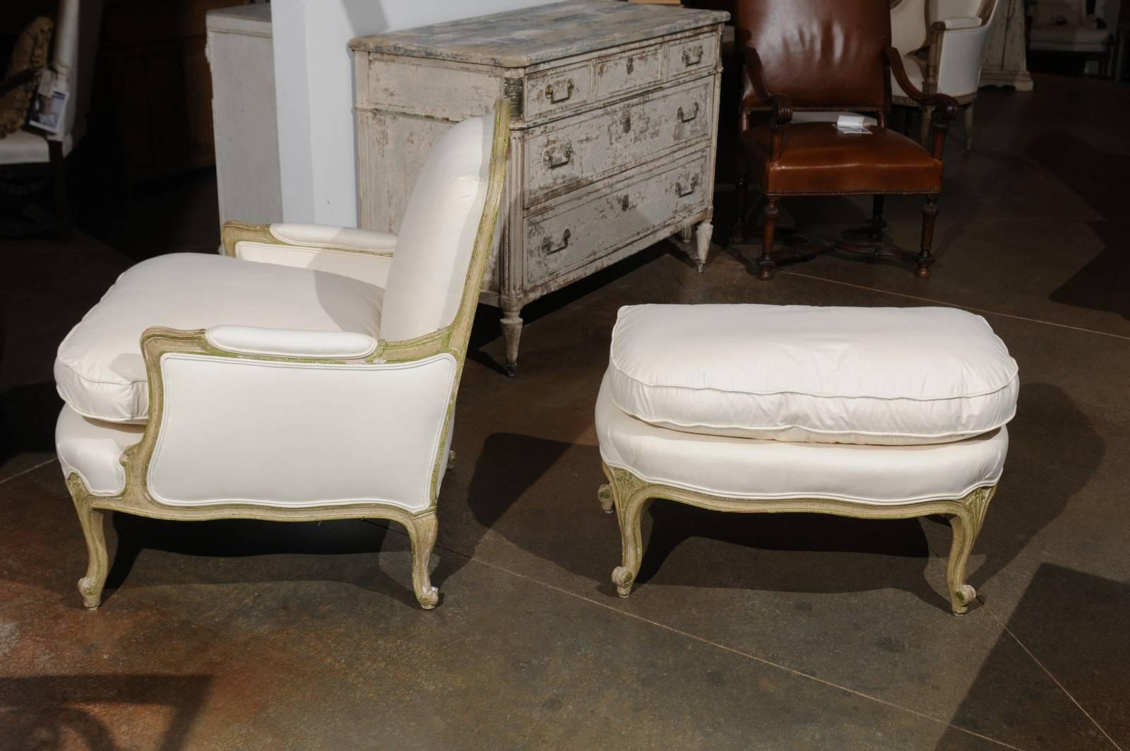A French Louis XV period painted wood bergère chair with its ottoman from the mid-18th century with new upholstery. This French bergère chair features a light grey green painted body made of a slightly slanted back and partially upholstered arms.